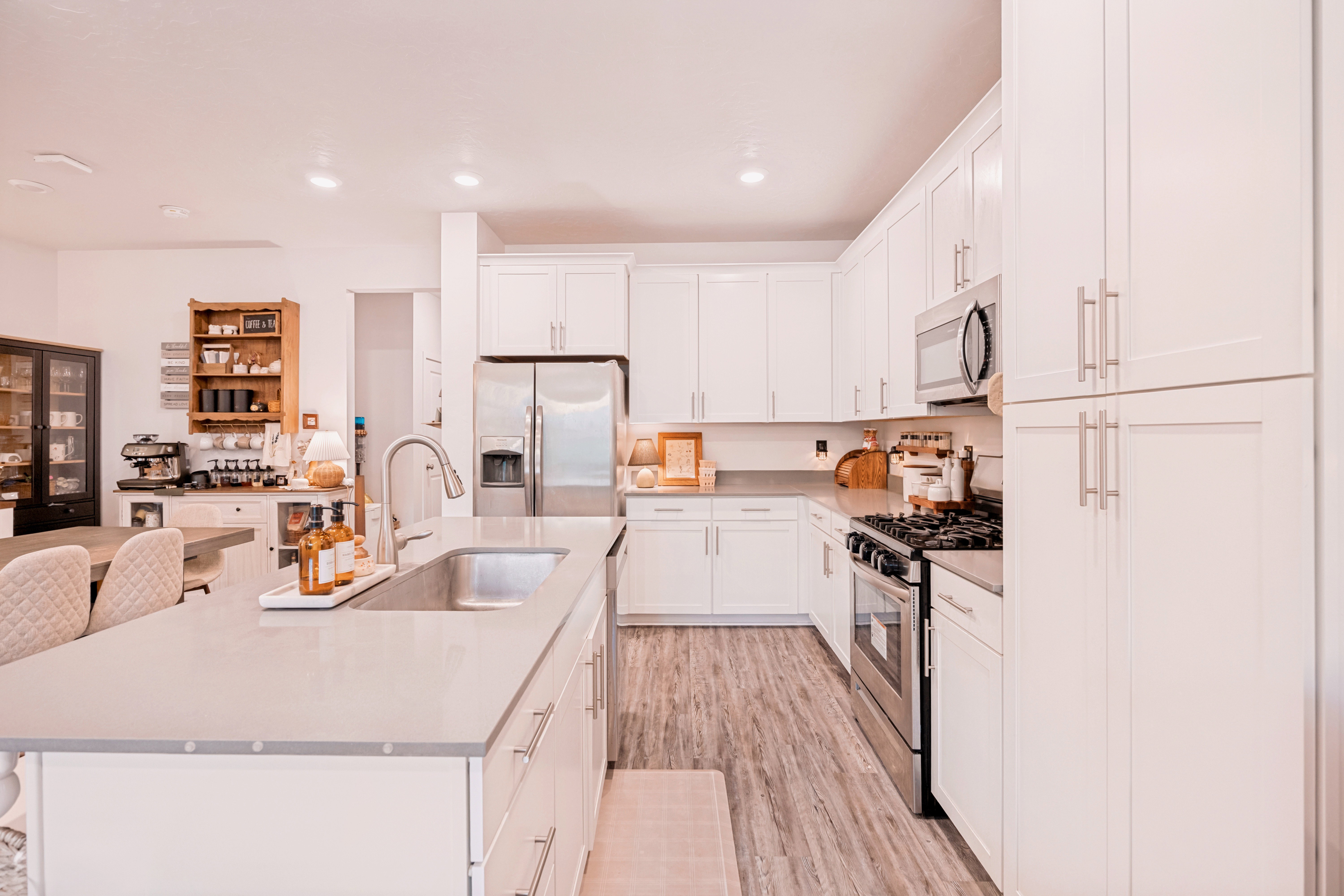 Spacious kitchen featuring white cabinetry, stainless steel appliances, a large center island with an undermount sink, light-toned countertops, and wood-finish flooring