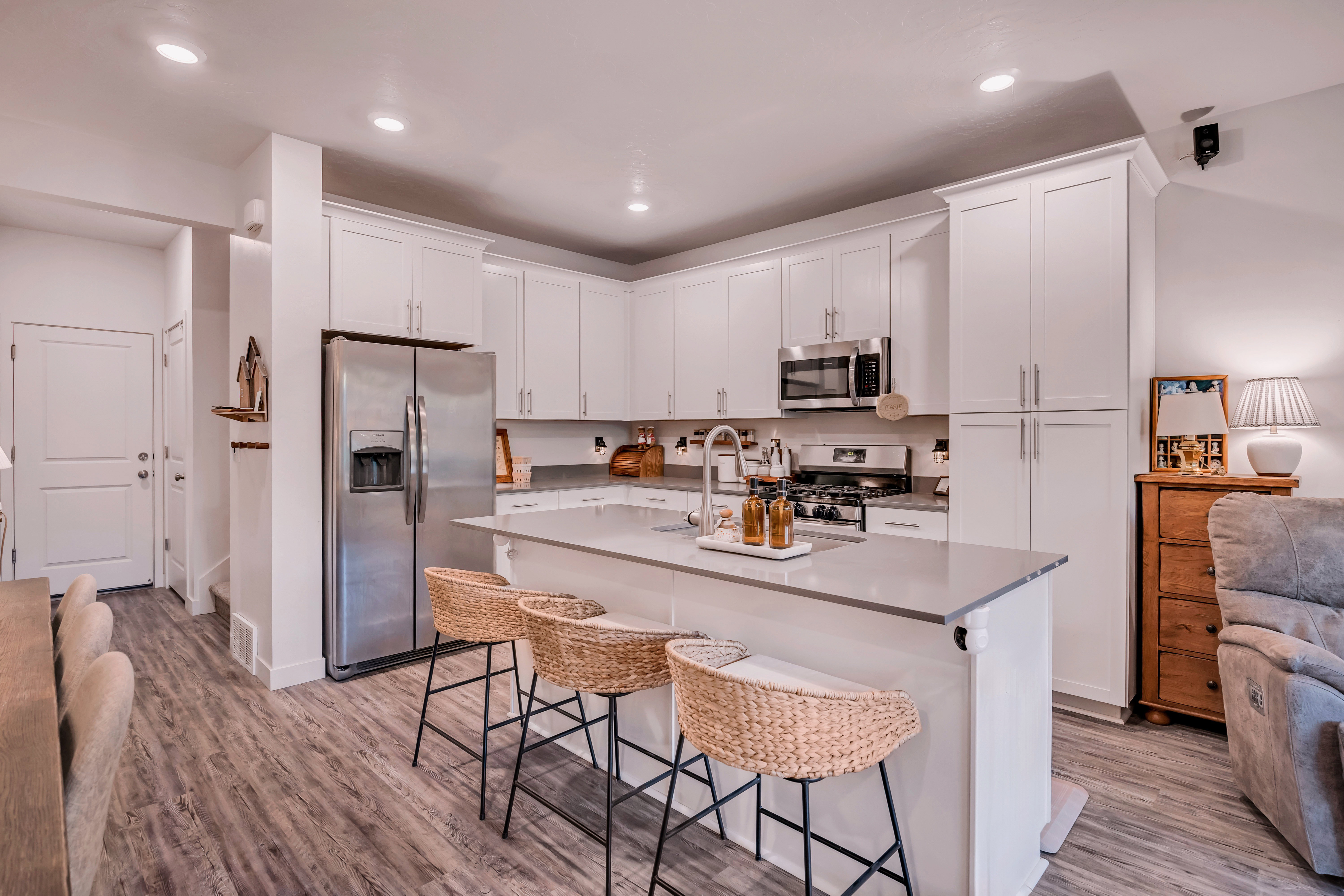 Contemporary kitchen featuring white shaker cabinetry, stainless steel appliances, a large center island with seating, and wood-finish flooring