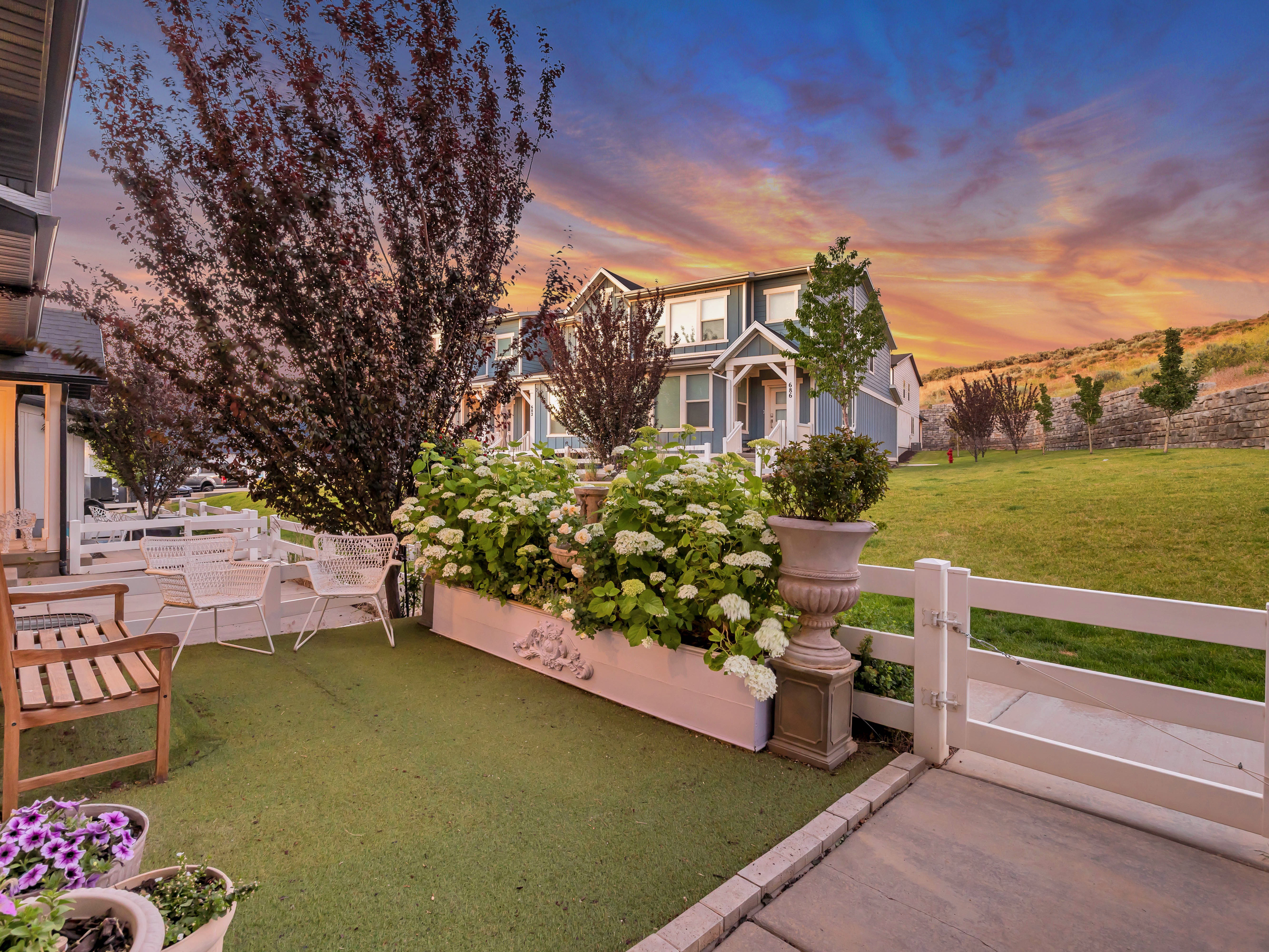 Exterior patio featuring artificial turf, a white planter box with flowering shrubs, and a white picket fence