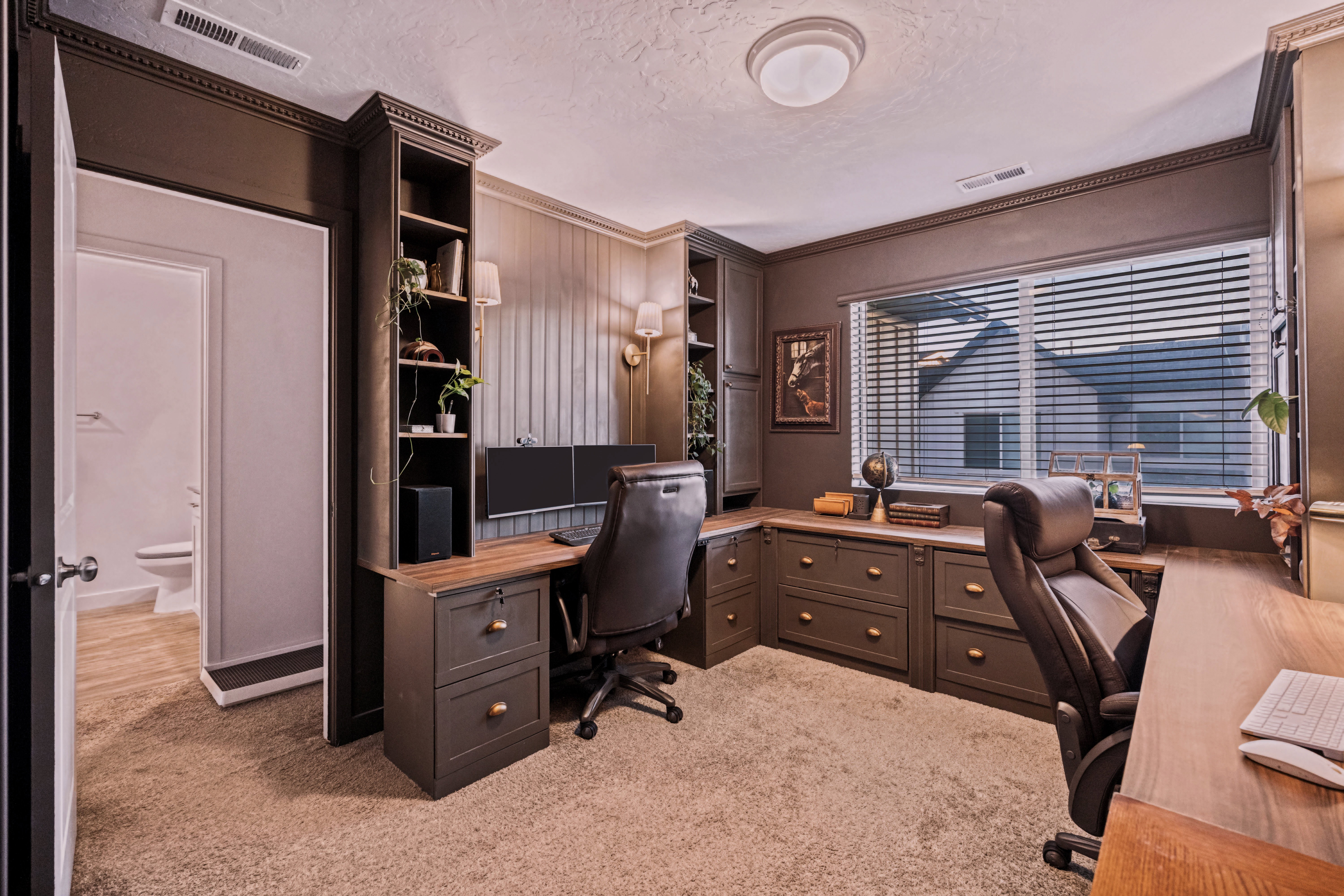 Dedicated office space featuring extensive built-in cabinetry, wood-finish countertops, wall paneling, and a window with blinds