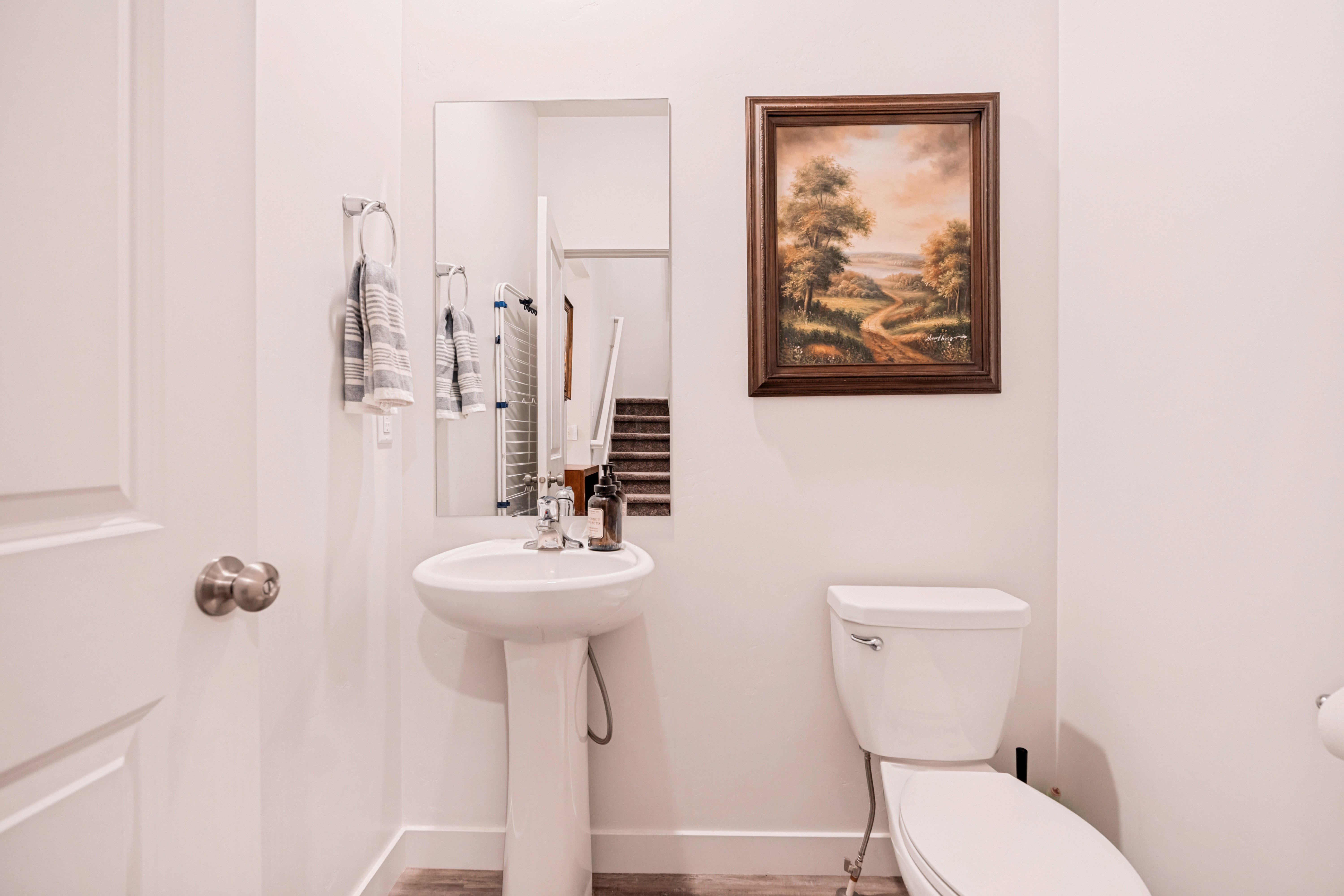 White pedestal sink with a chrome faucet, wall-mounted mirror, and wood-finish flooring