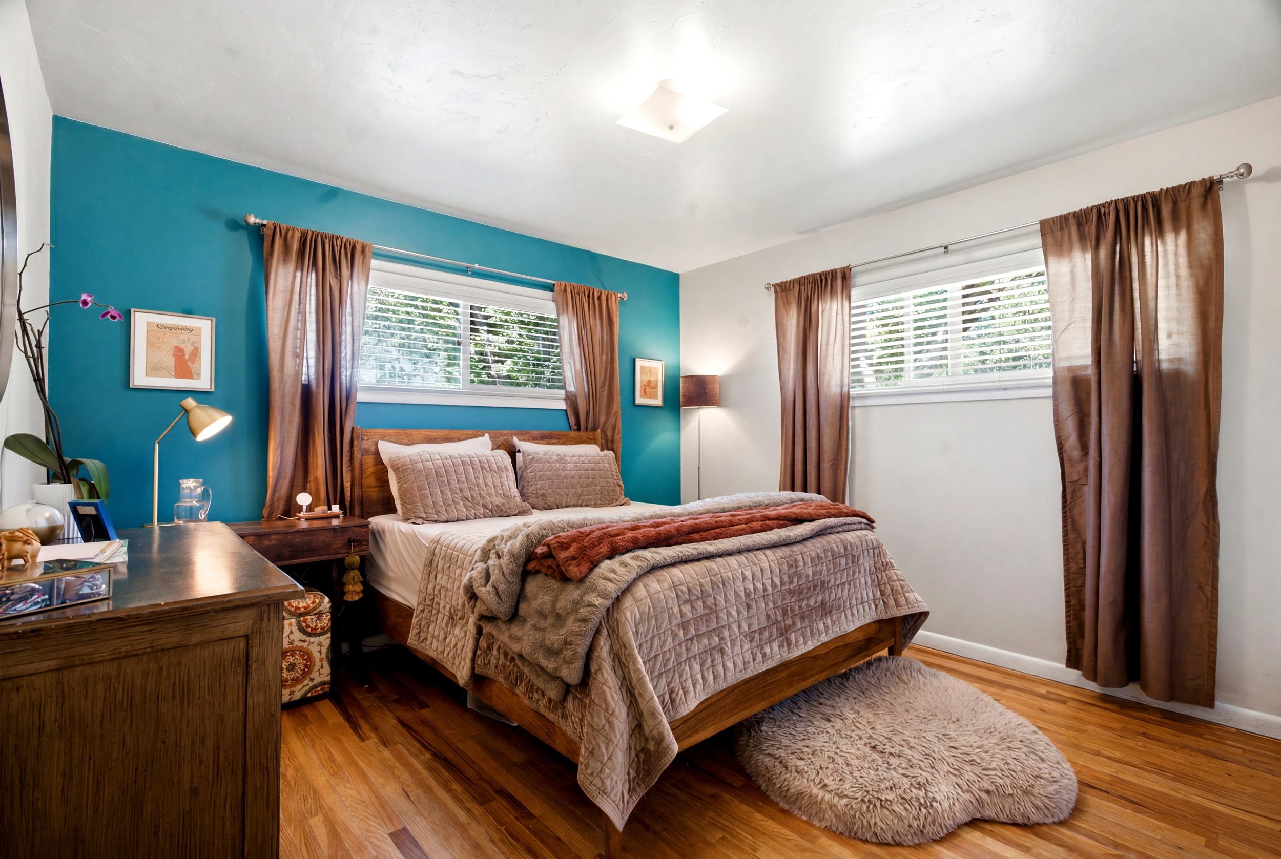 Bedroom featuring wood-finish flooring, a vibrant accent wall, two windows with blinds, and a built-in overhead light fixture