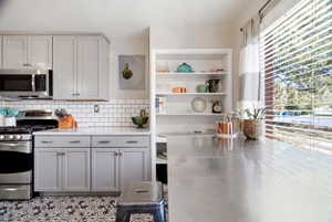 Well-appointed kitchen featuring light gray cabinetry, stainless steel appliances, a white subway tile backsplash, and patterned floor tiling