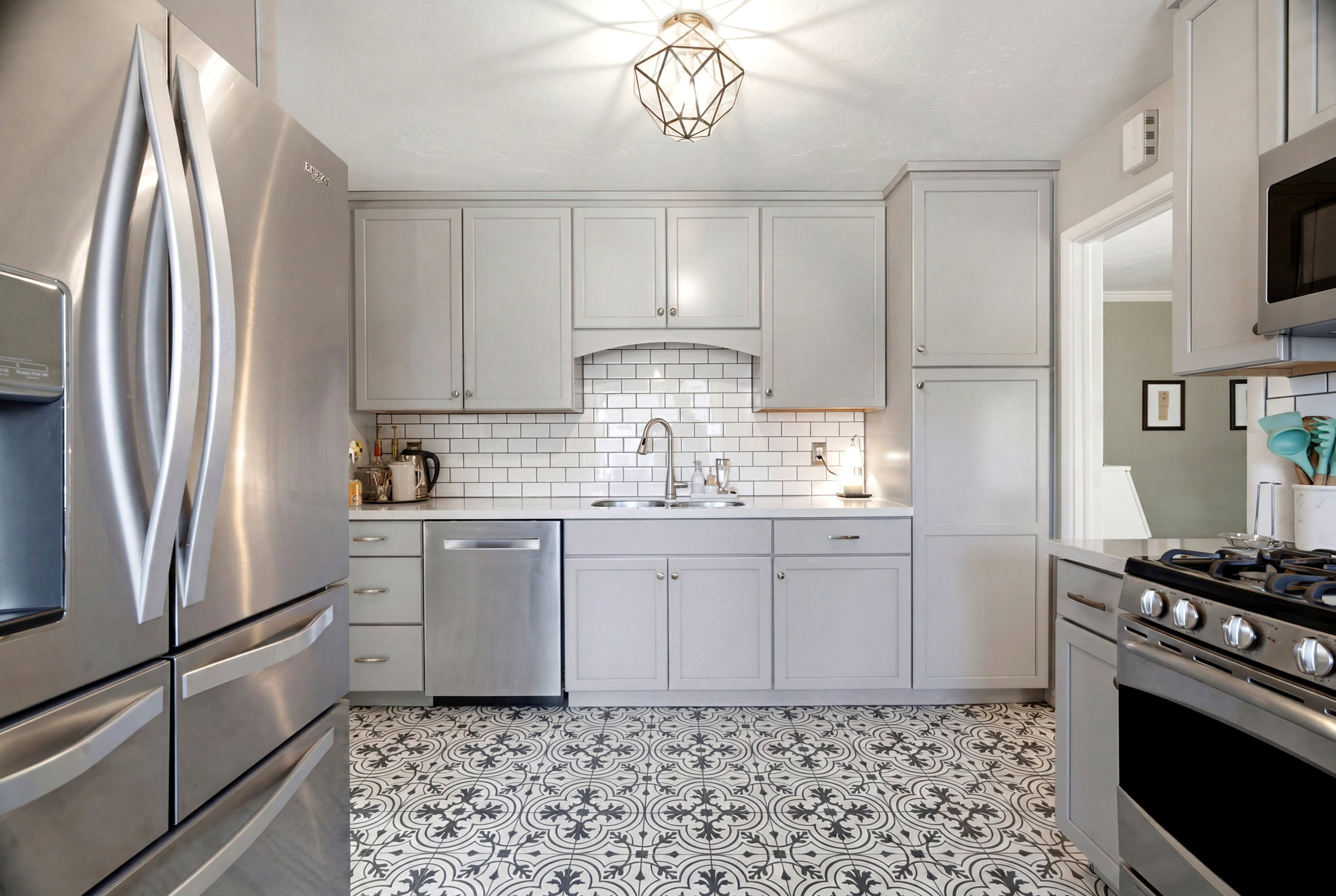 Kitchen featuring light gray cabinetry, subway tile backsplash, patterned floor tiling, stainless steel appliances, and a recessed sink