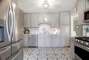 Kitchen featuring light gray cabinetry, subway tile backsplash, patterned floor tiling, stainless steel appliances, and a recessed sink