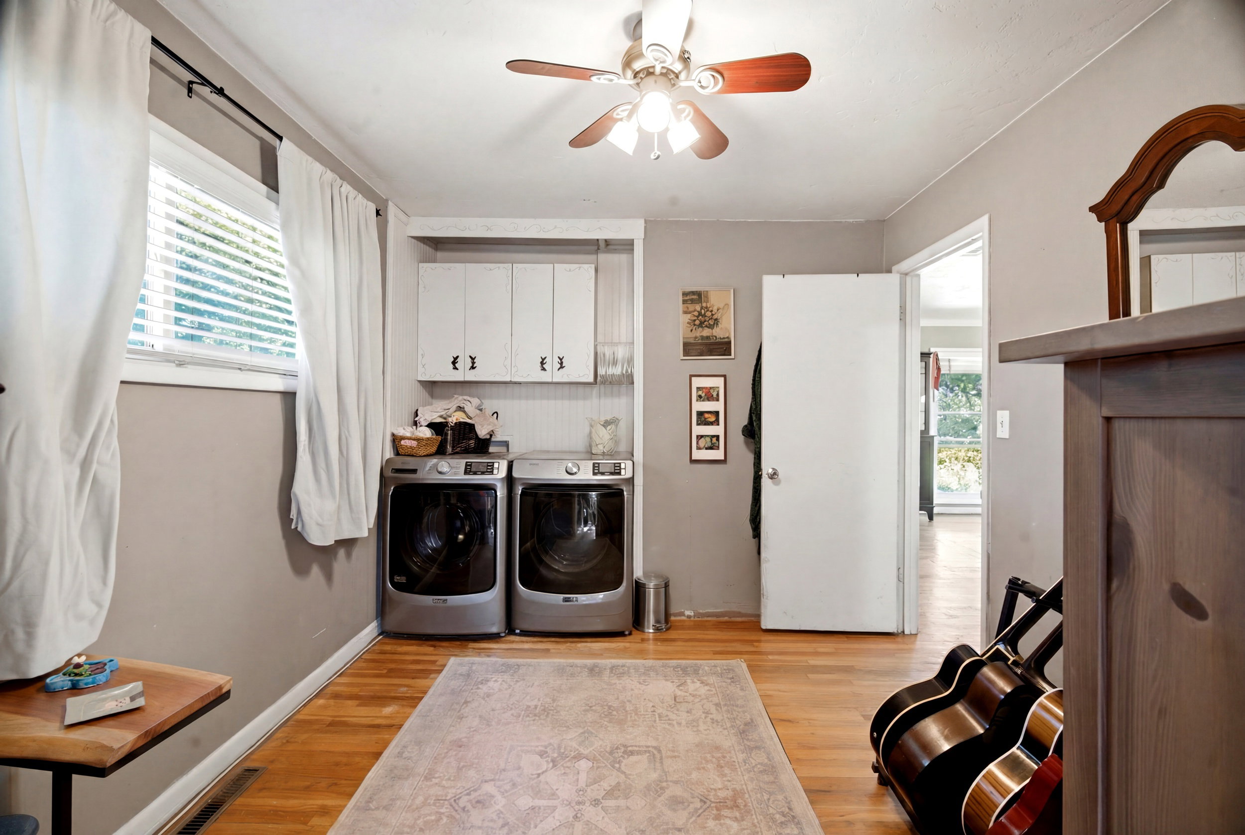 Dedicated laundry area featuring a window, hardwood-finish flooring, overhead cabinetry, a ceiling fan, and beadboard paneling