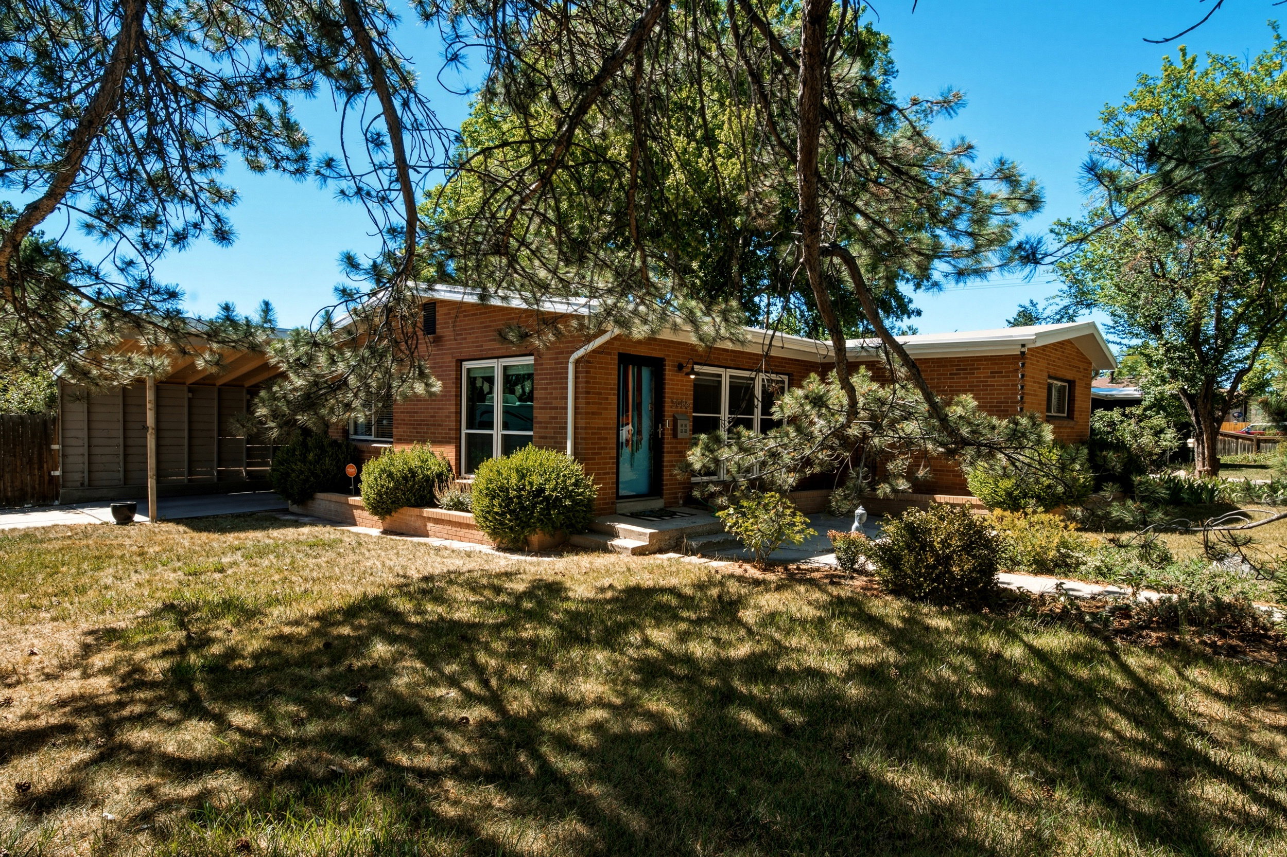 Brick facade home featuring a carport, mature trees, and established landscaping