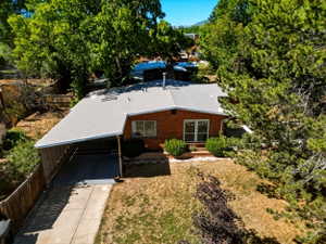 Brick exterior residence featuring a carport, mature perimeter trees, and a front yard with established shrubs