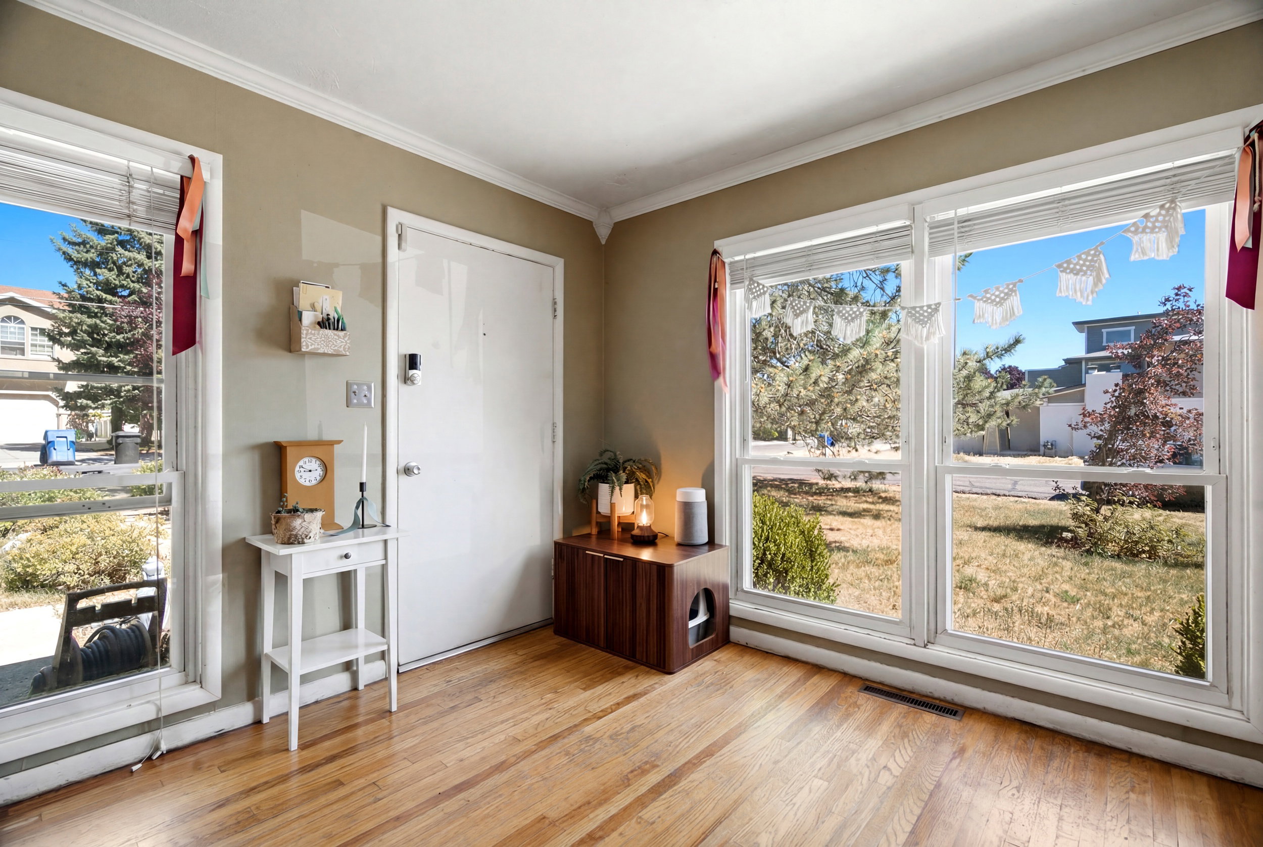 Hardwood flooring extending through a room with multiple large windows, crown molding, and a solid white entry door