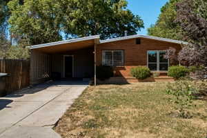 Brick exterior with a covered carport featuring wood-finish ceiling panels, a concrete driveway, and front landscaping