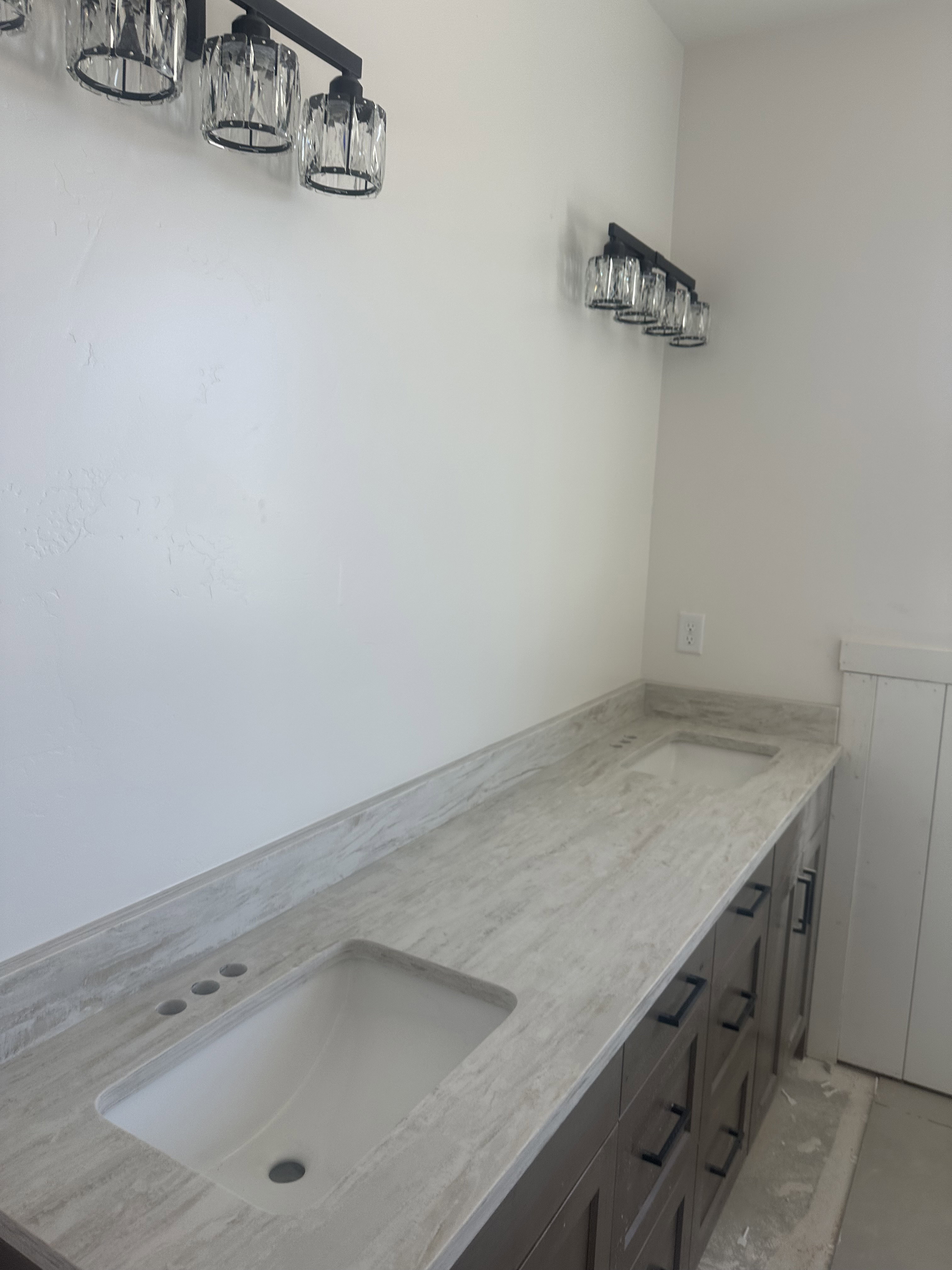 Dual vanity with light-toned countertop, integrated sinks, dark wood-finish cabinetry, and contemporary black hardware