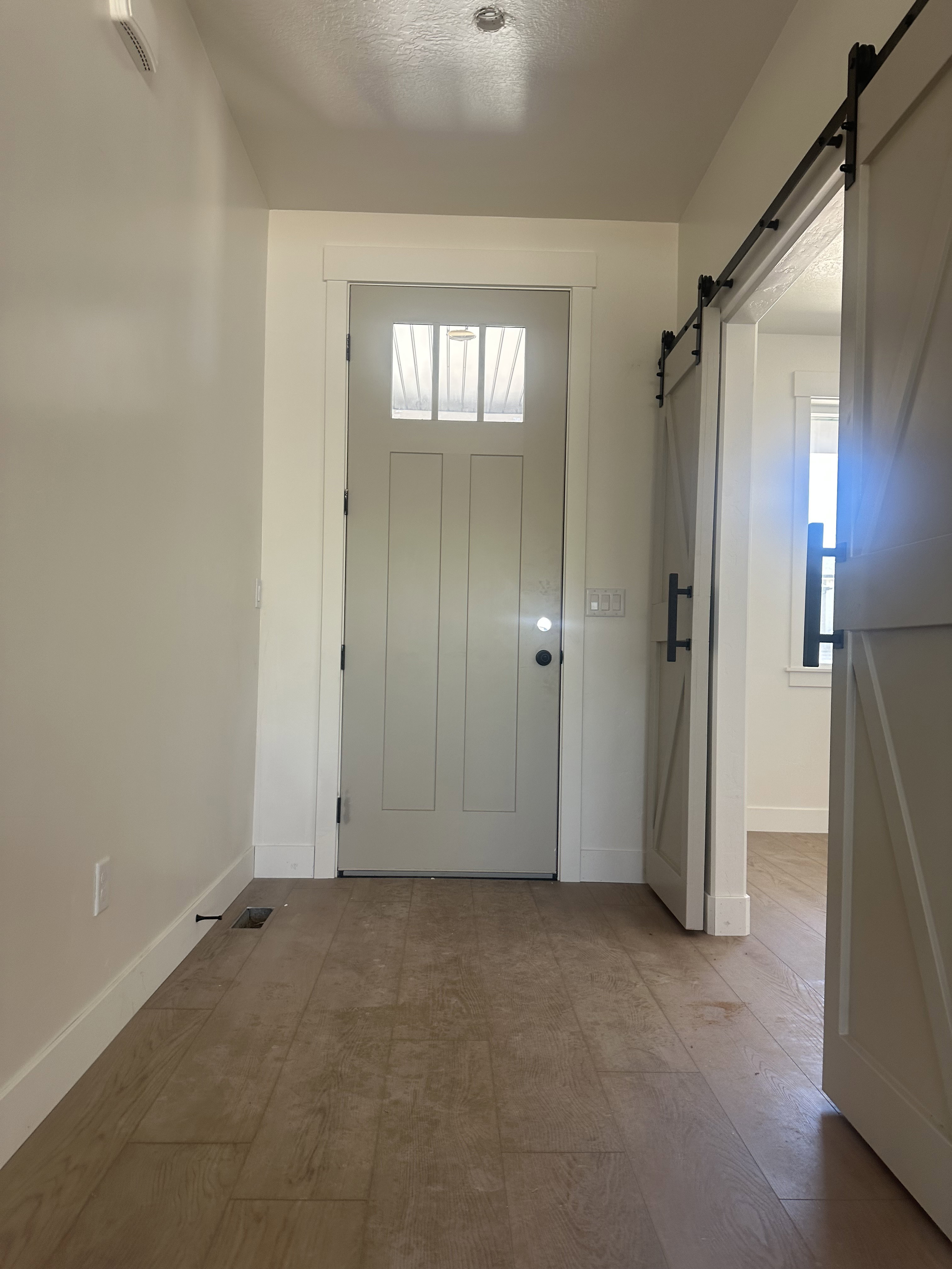 Entryway featuring wood-finish flooring, a contemporary front door with transom lites, and a barn door with black hardware