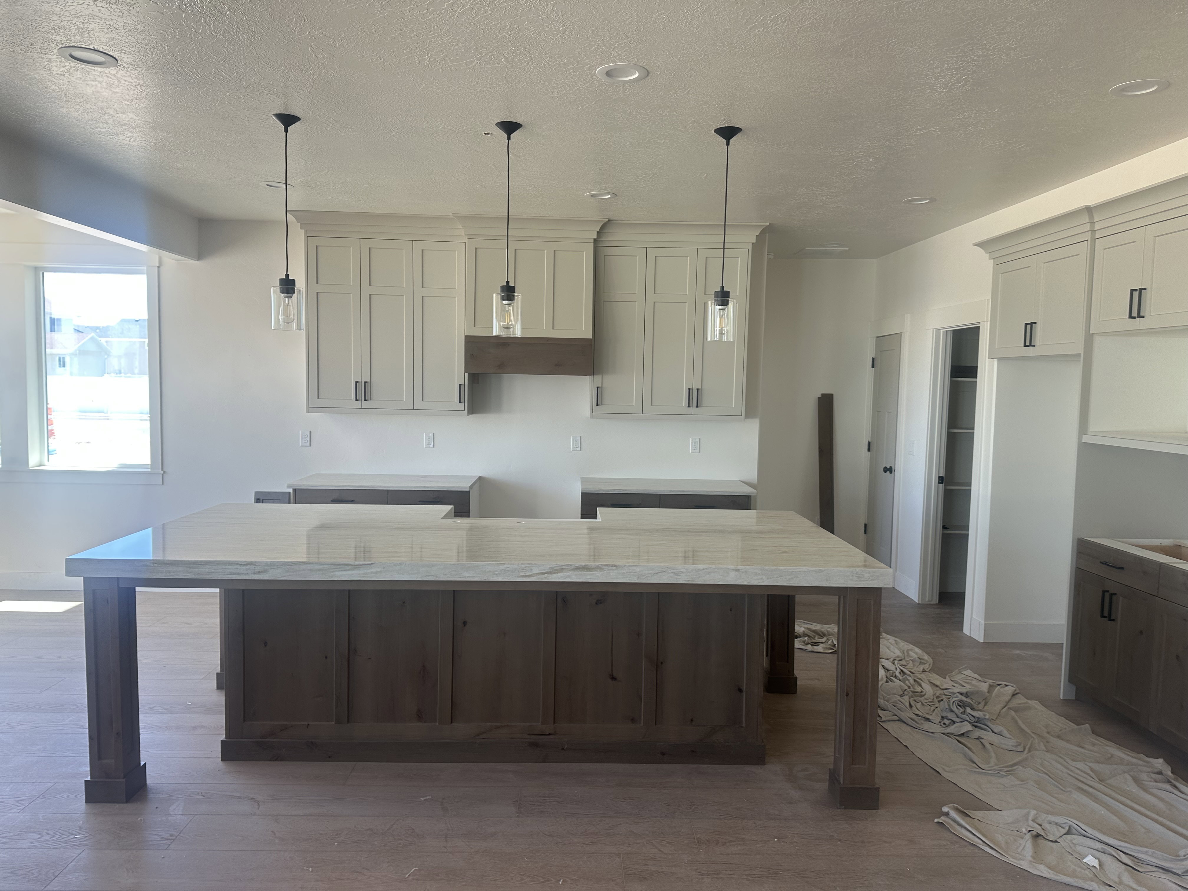 Spacious kitchen featuring a large island with a light-toned countertop, pendant lighting, shaker-style cabinetry, and wood-finish flooring