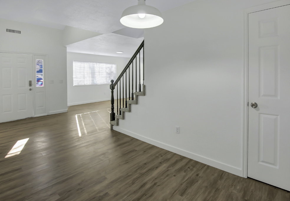 Entry foyer featuring a white paneled door with decorative glass inserts, wood-finish flooring, a contemporary pendant light fixture, and a staircase with a dark wood-finish handrail and black balusters