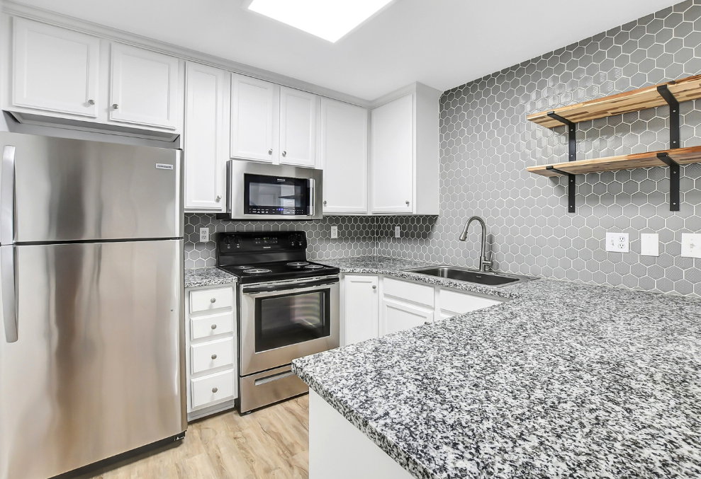 Kitchen featuring white cabinetry, stainless steel appliances, granite-style countertops, gray hexagonal tile backsplash, and light wood-finish flooring