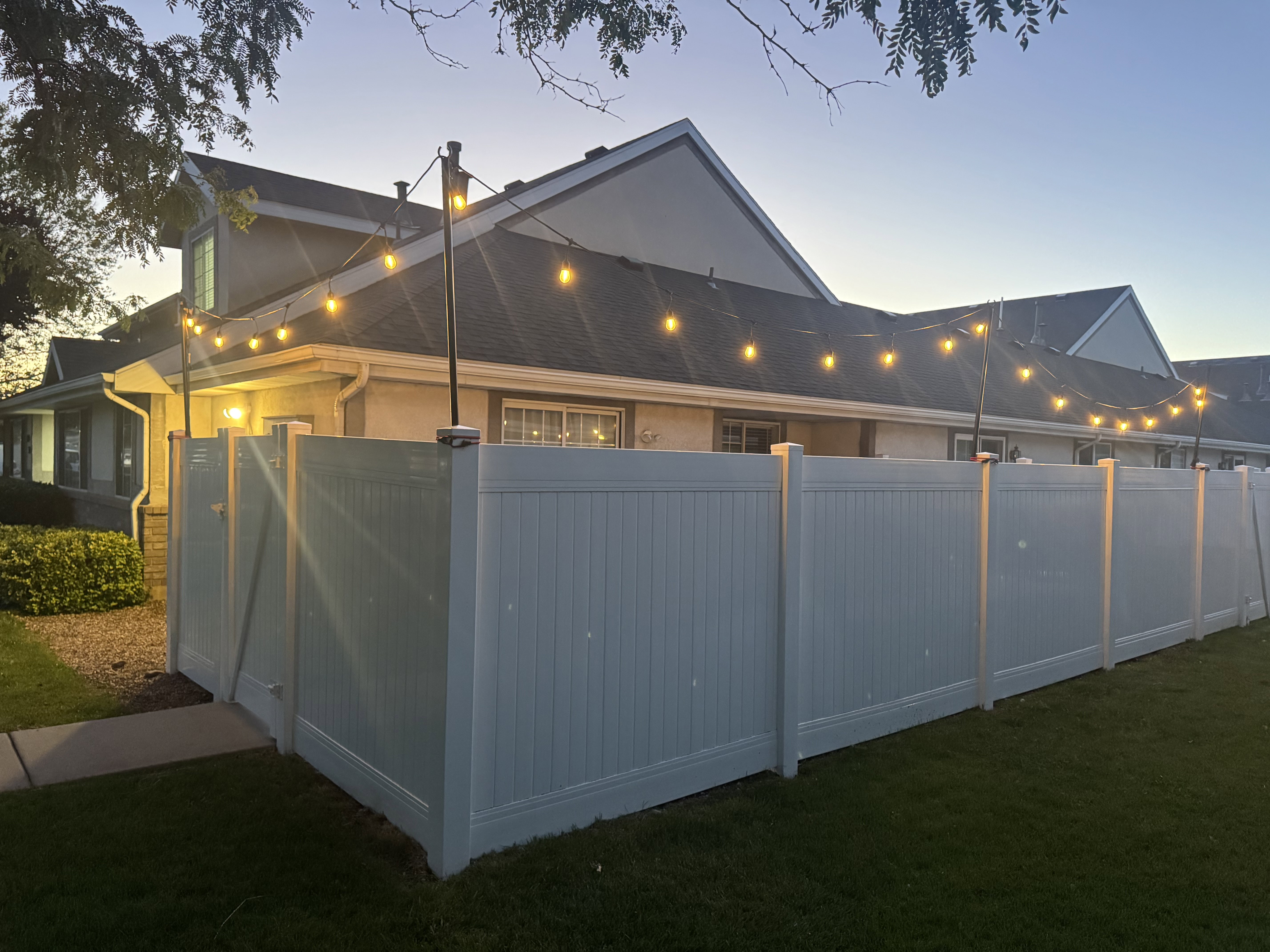 Private backyard featuring a white privacy fence, a manicured lawn, and string lighting
