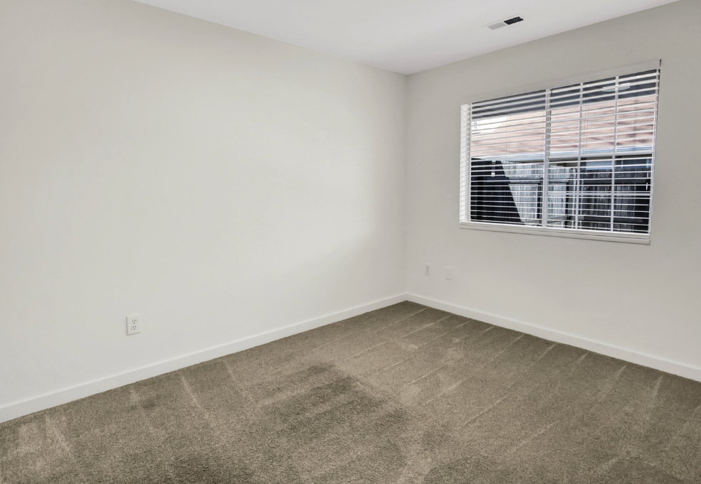 Bright room featuring neutral-toned walls, a window with horizontal blinds, and clean carpeting