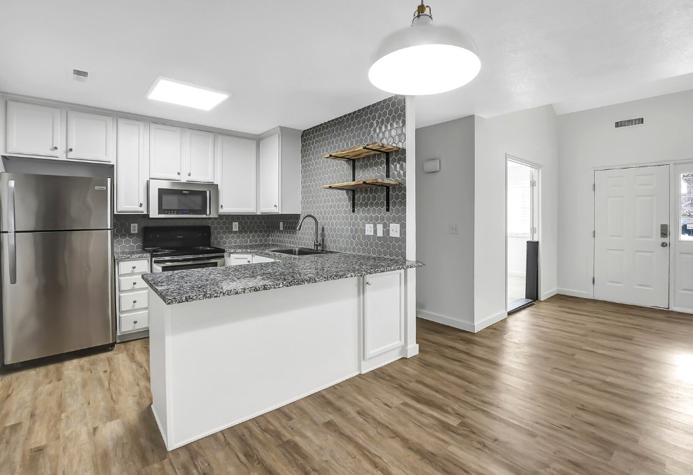 Open-concept kitchen with white cabinetry, stainless steel appliances, granite-style countertops, and hexagon tile backsplash