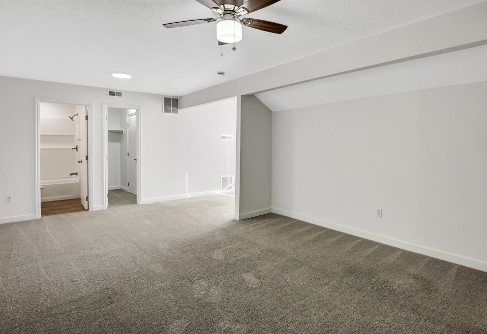 Spacious room featuring neutral carpet flooring, white walls, a ceiling fan with integrated lighting, and white baseboards