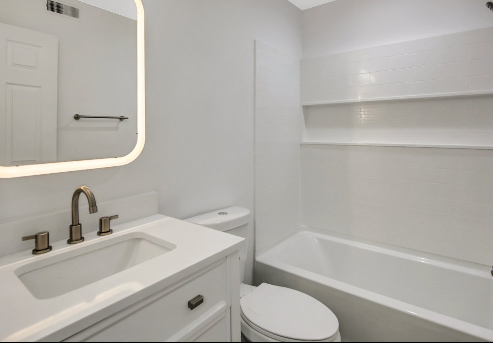 Bathroom featuring a white vanity with an integrated sink, brushed bronze faucet, and an illuminated mirror