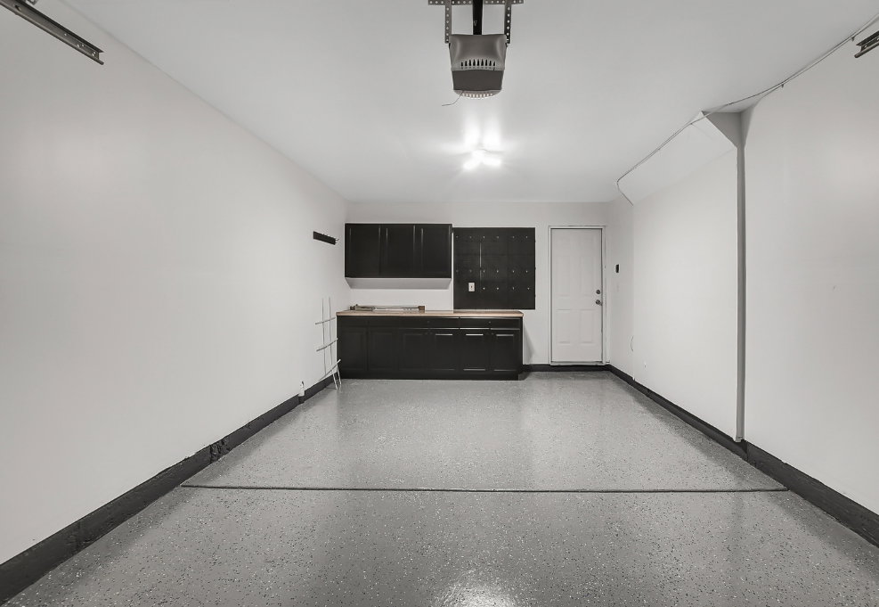 Garage space featuring an epoxy-coated floor, built-in dark cabinetry with a wood-finish countertop, and a white entry door