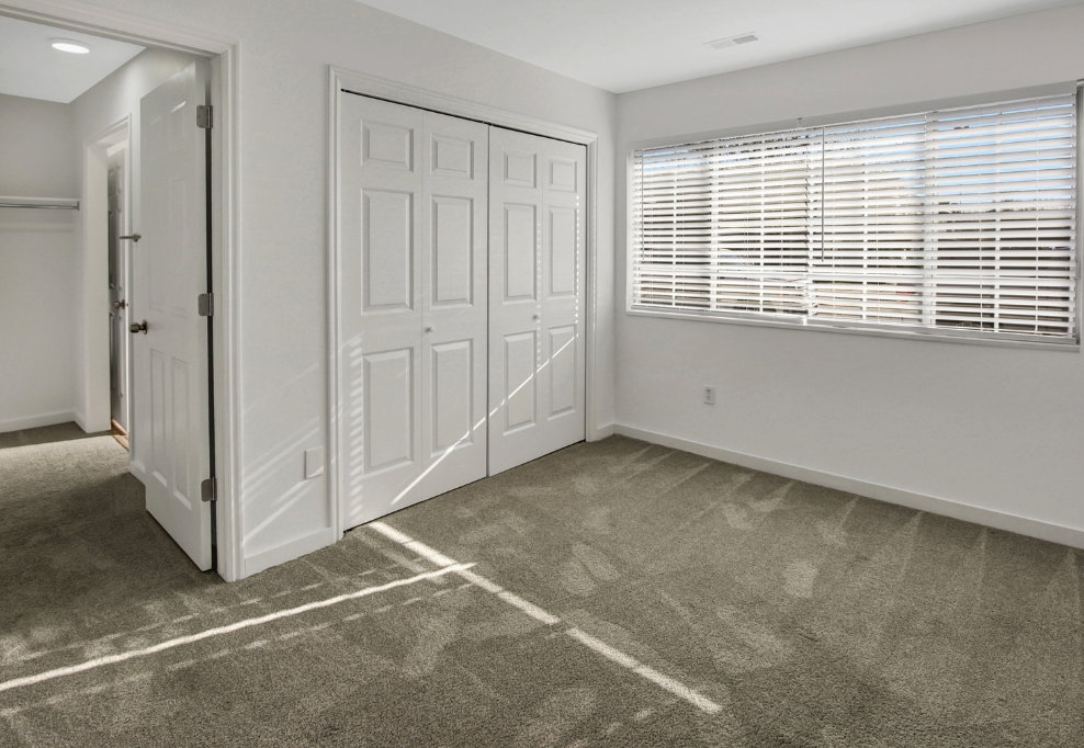 Carpeted room featuring a double bi-fold closet, white interior doors, and a window with horizontal blinds