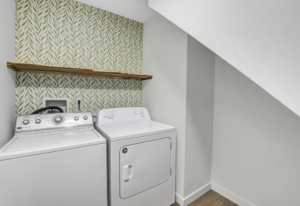 Laundry area featuring patterned wallpaper, a rustic wood shelf, and wood-finish flooring