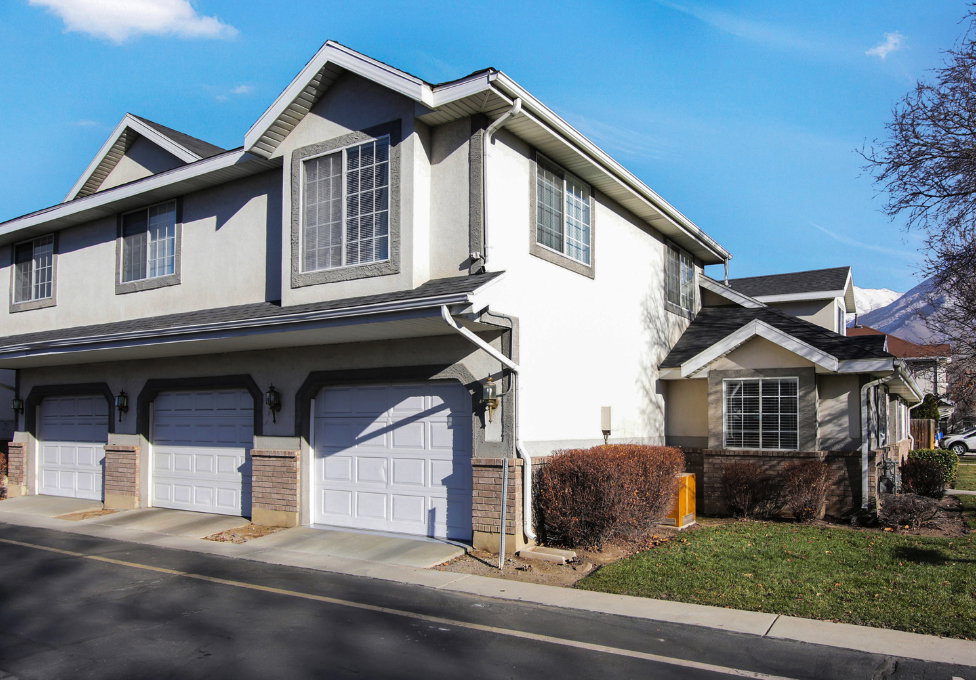 Multi-level exterior featuring light-colored siding, multiple garage doors, and dark shingle roofing