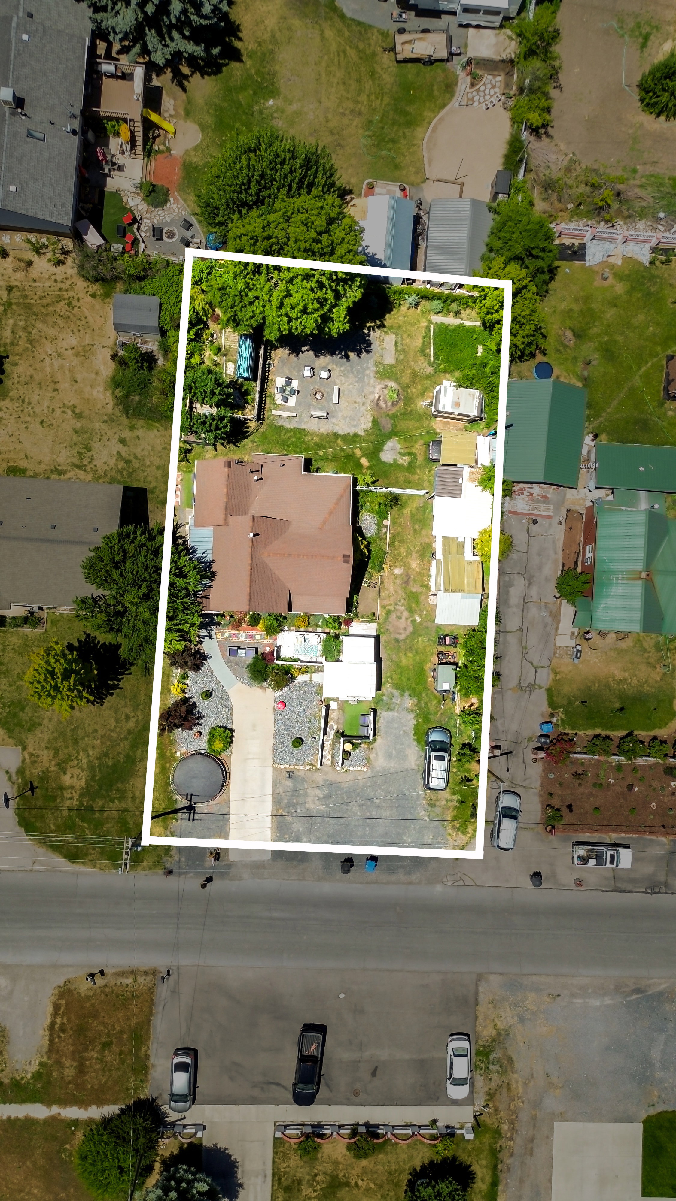 Aerial view of a property featuring a brown-roofed residence, extensive gravel parking, a winding paved driveway, and a backyard with a fire pit area