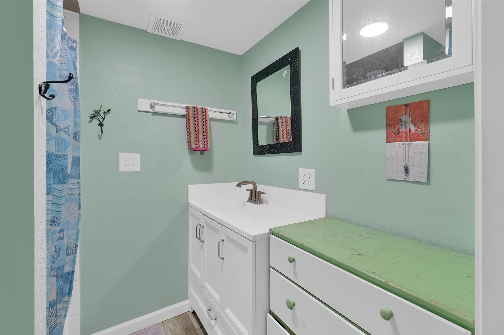 Bathroom featuring a white vanity with integrated sink, brushed nickel faucet, a framed mirror, and wood-finish flooring