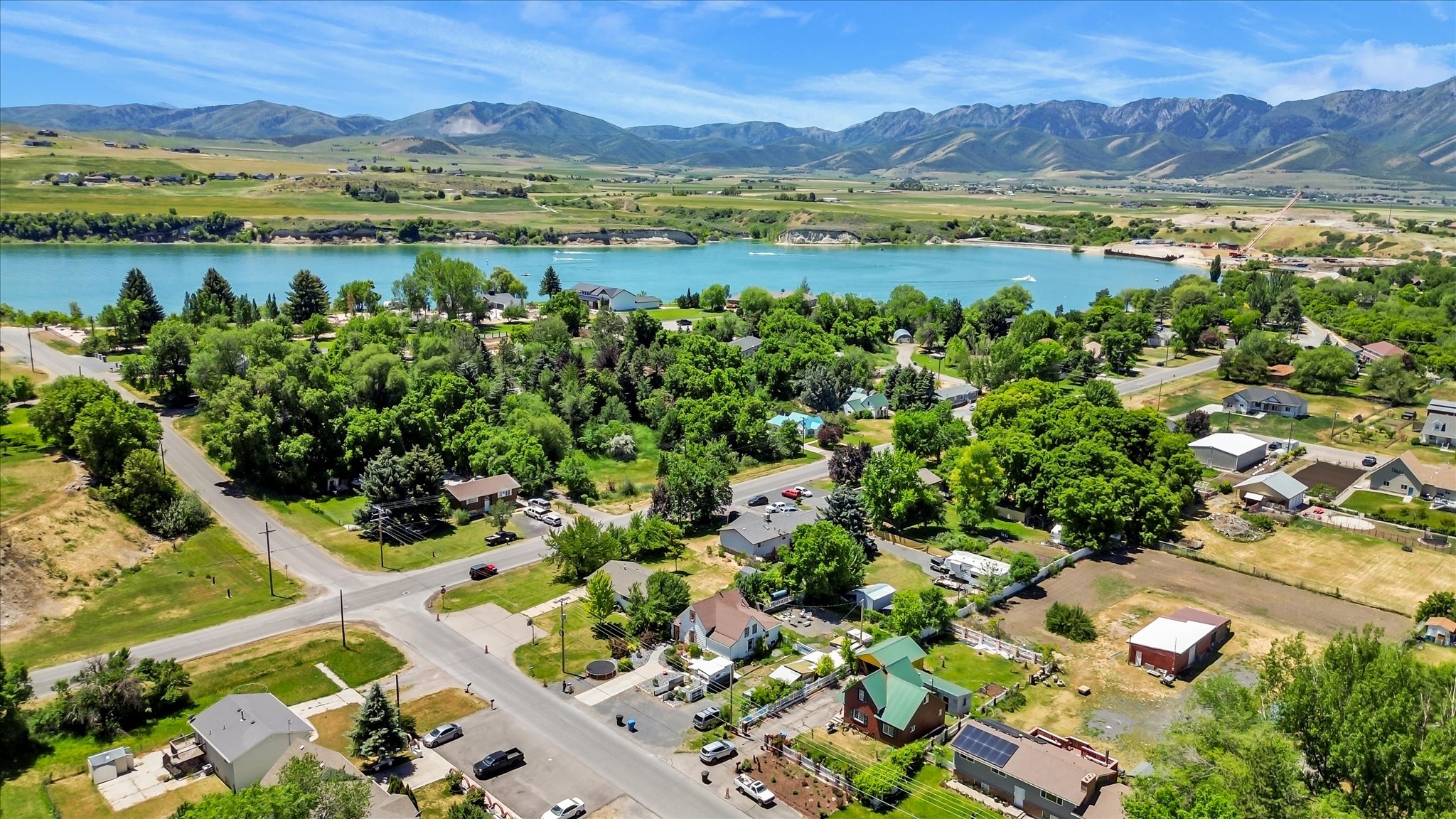 Expansive aerial perspective showcasing a residential area with a prominent body of water, surrounded by green landscapes and distant mountains