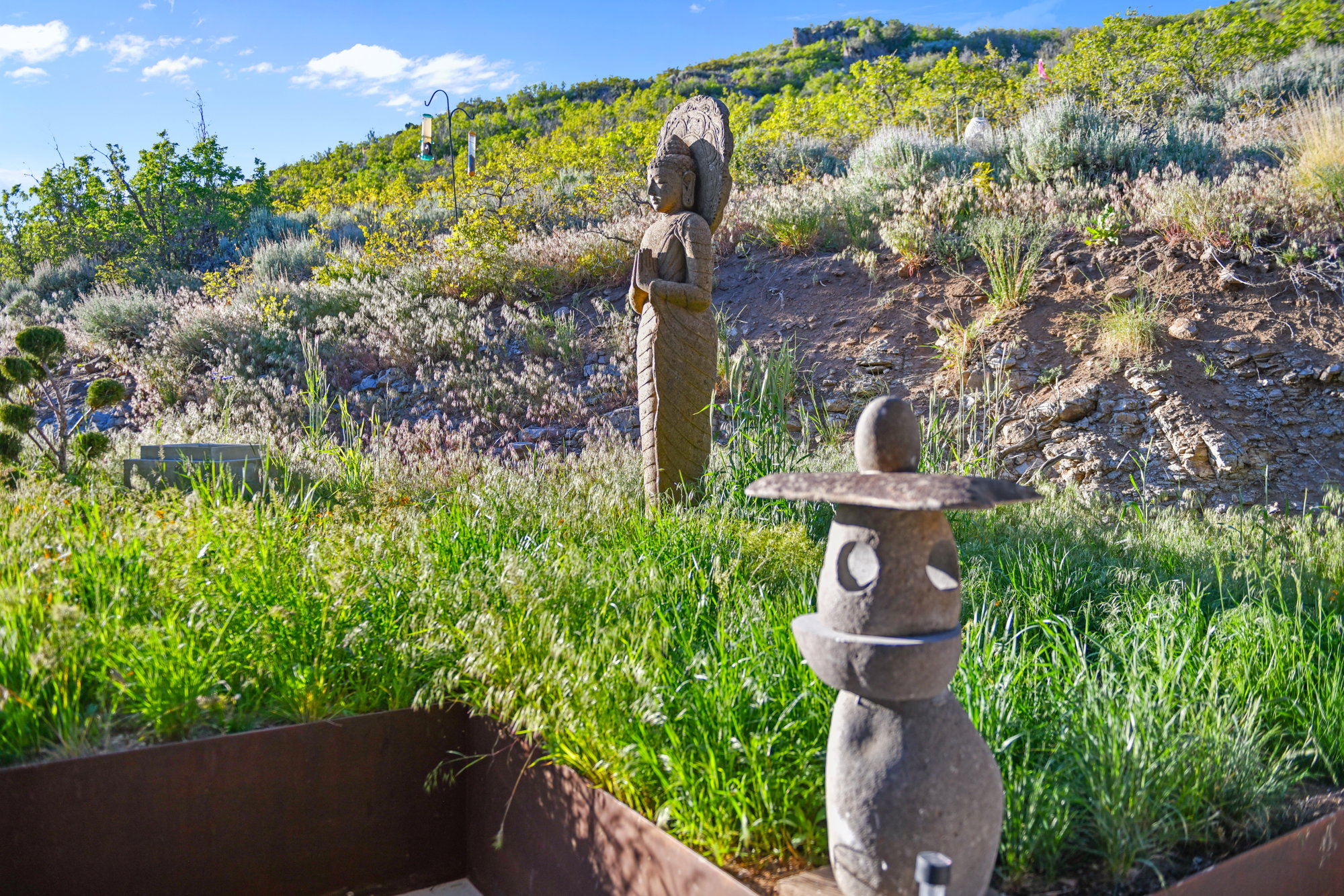 Landscaped hillside featuring natural vegetation, stone sculptures, and a clear blue sky