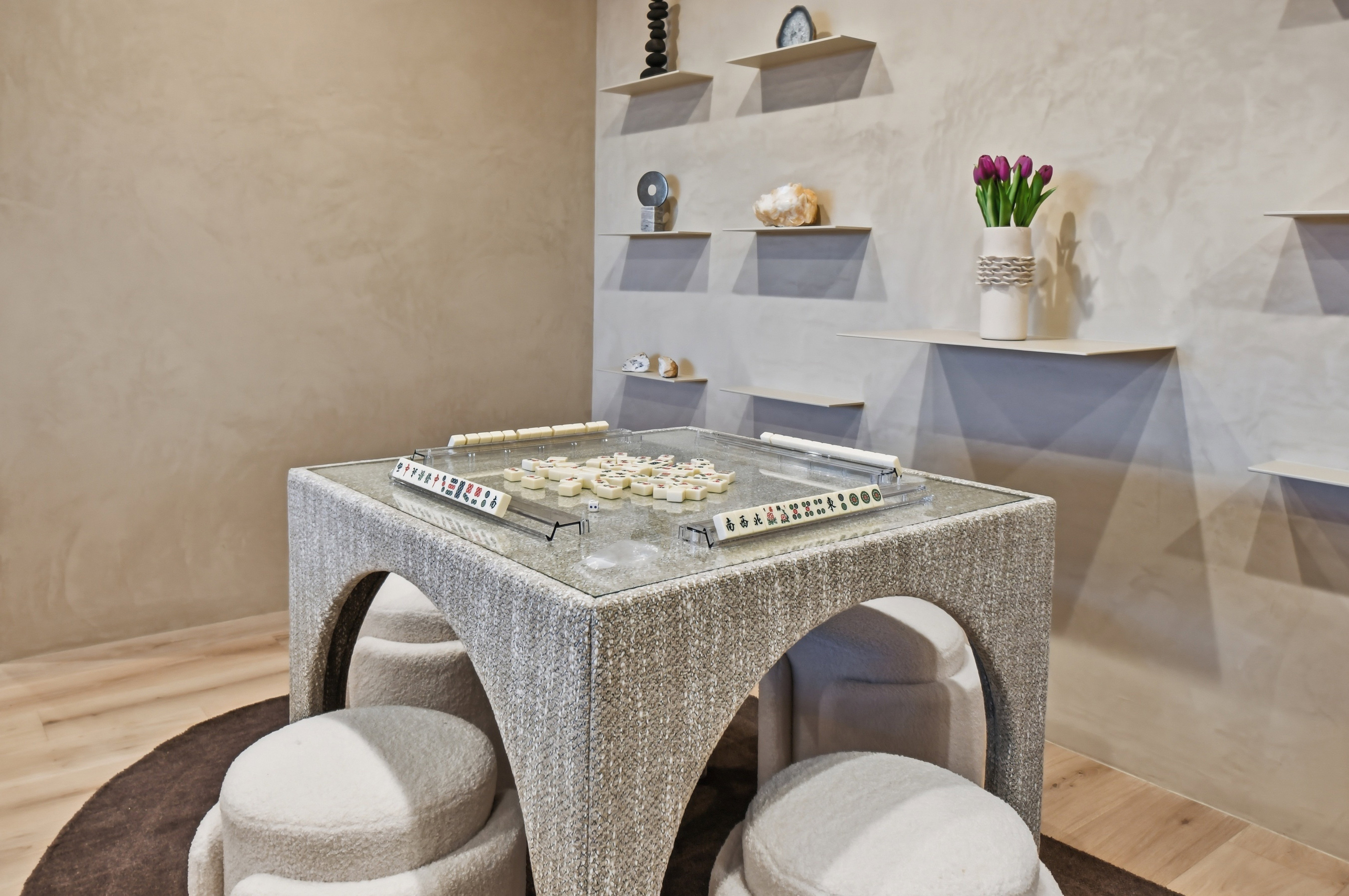 Textured wall finish, wood-finish flooring, built-in floating wall shelves, and a fabric-wrapped table with a glass top