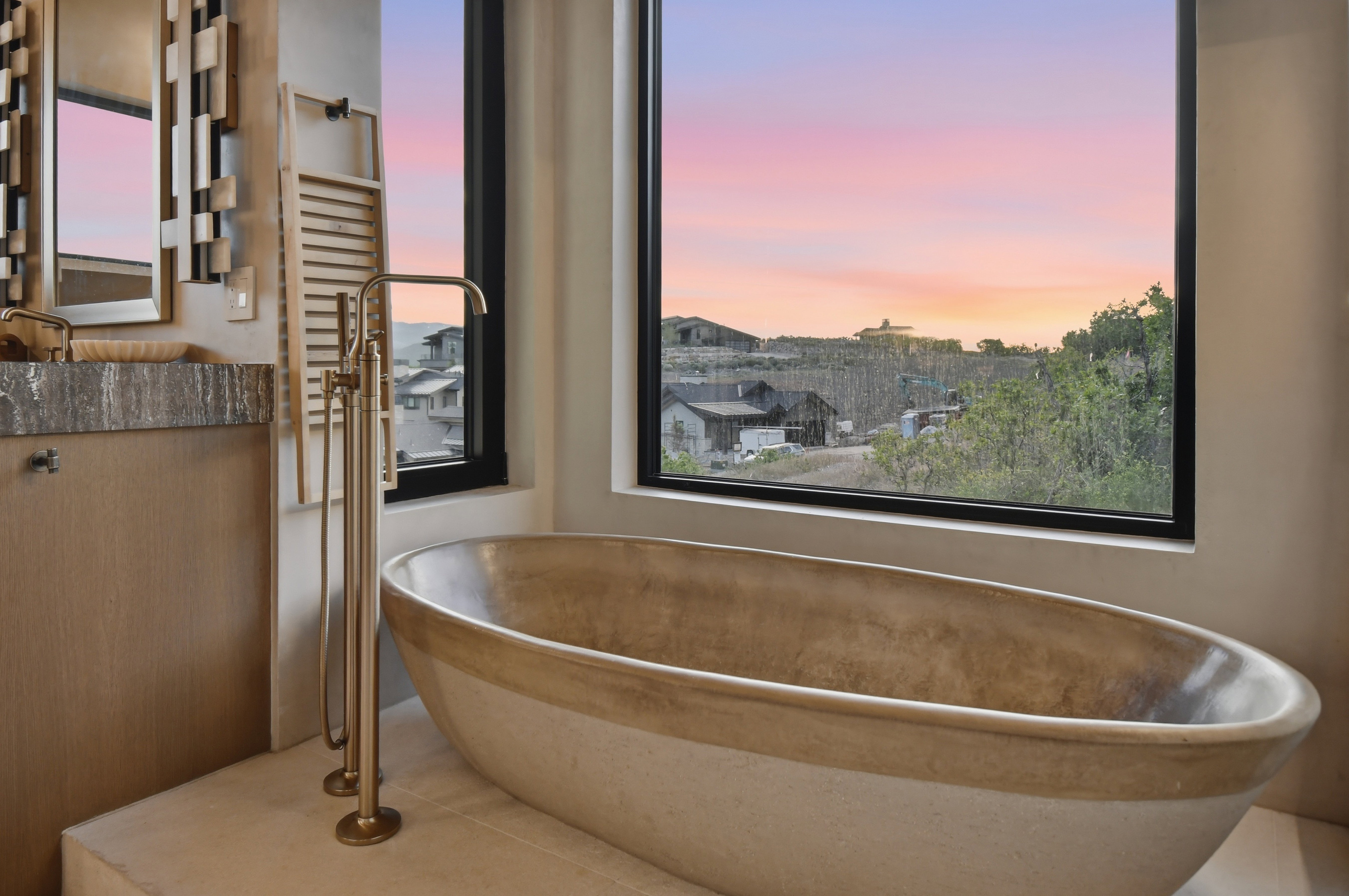 Free-standing soaking tub with a floor-mounted bronze faucet, set against a large picture window