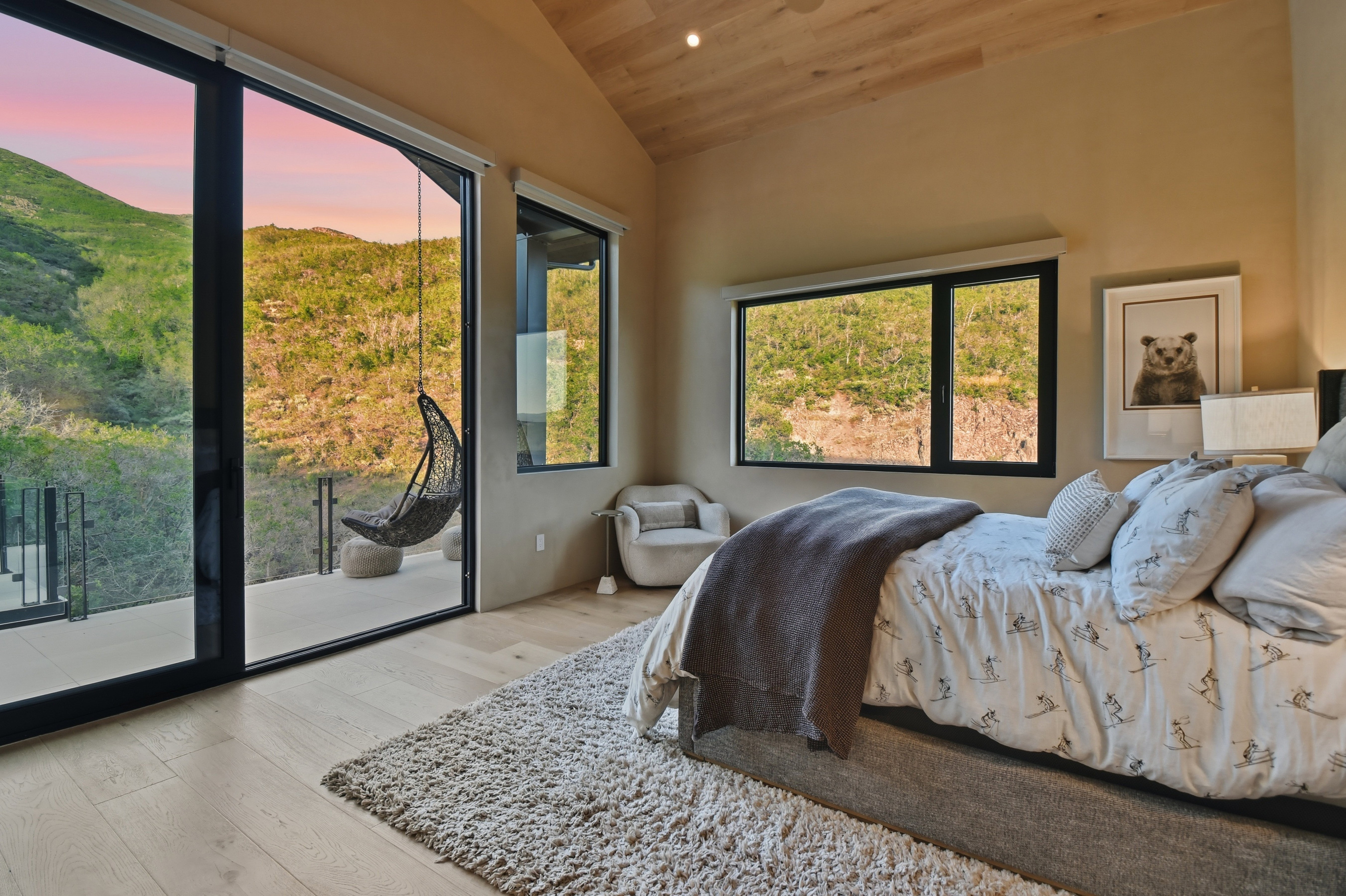 Expansive room featuring a vaulted wood-finish ceiling, light wood-finish flooring, and large sliding glass doors opening to an outdoor balcony with glass railings