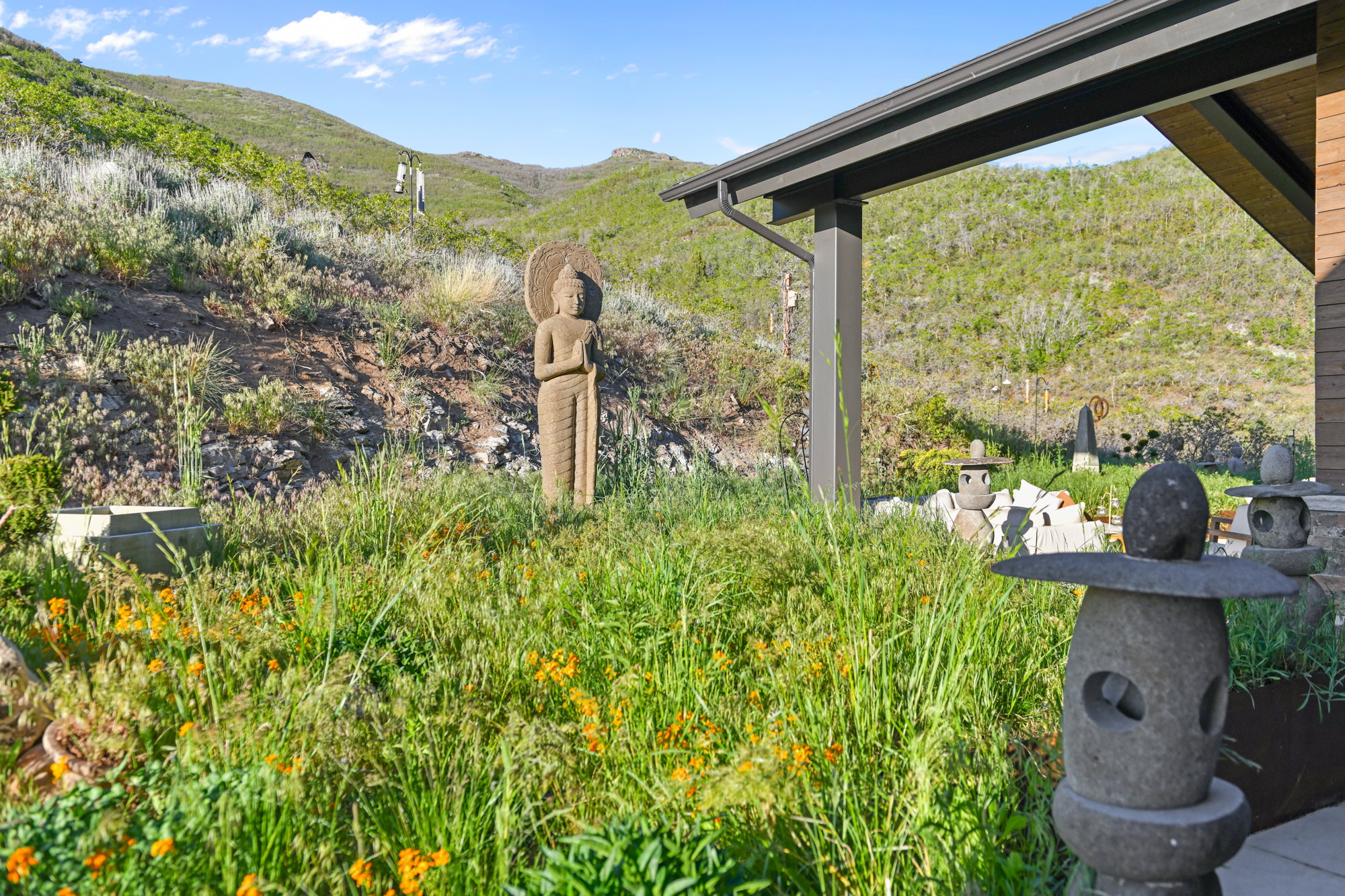 Outdoor landscaping featuring a stone statue, various stone garden lanterns, and native grasses with interspersed yellow wildflowers