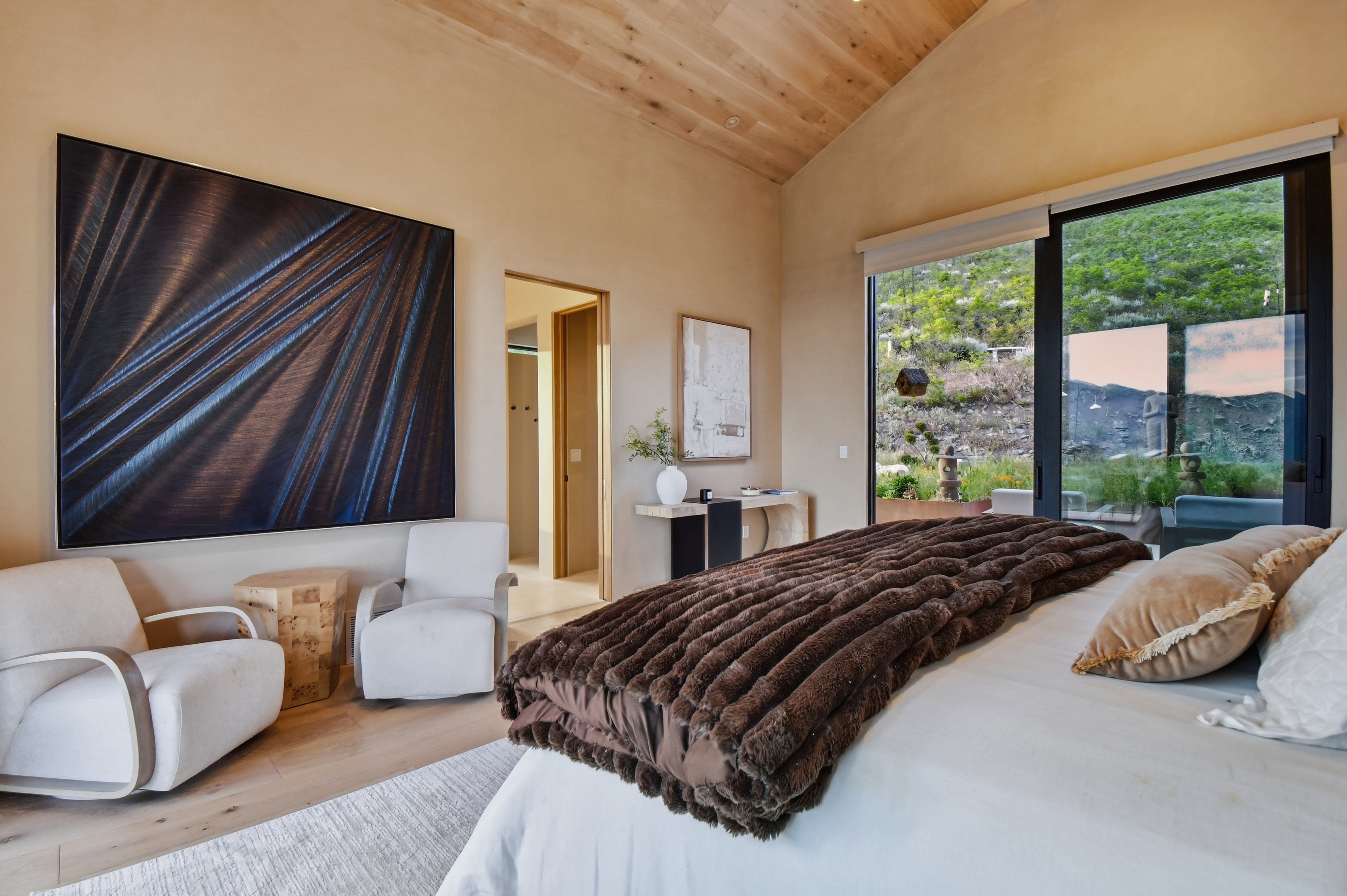 Vaulted wood-paneled ceiling, large sliding glass doors, light wood-finish flooring, neutral wall tones, and a recessed doorway