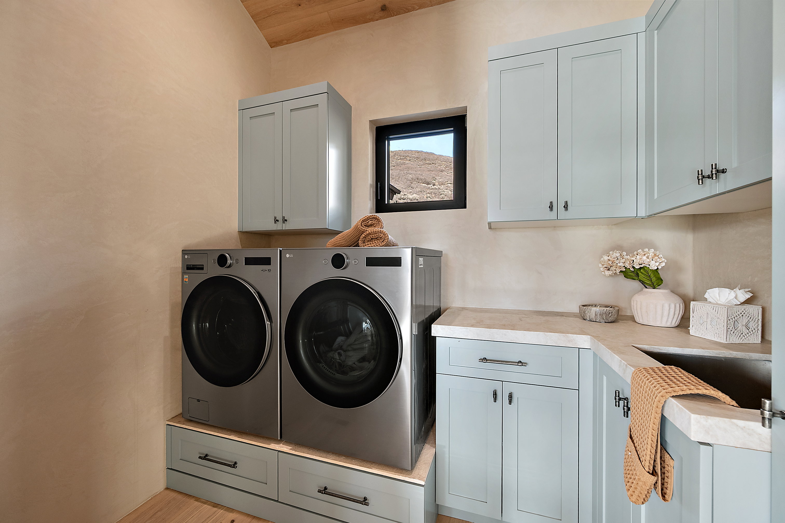 Dedicated laundry area featuring a sloped wood-paneled ceiling, light-toned walls, a built-in sink with a countertop, and light blue cabinetry with dark hardware