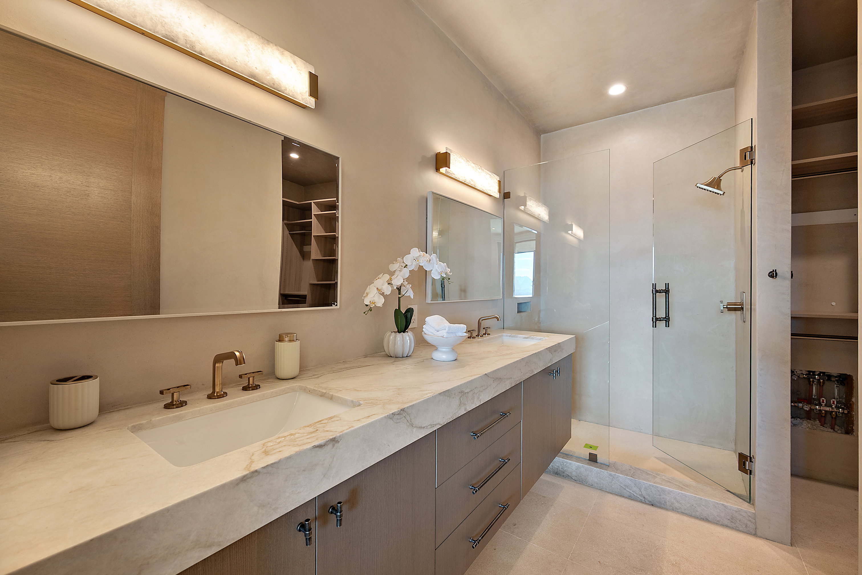 Dual vanity with integrated sinks, stone countertop, wood-finish cabinetry, frameless glass shower enclosure, and recessed lighting
