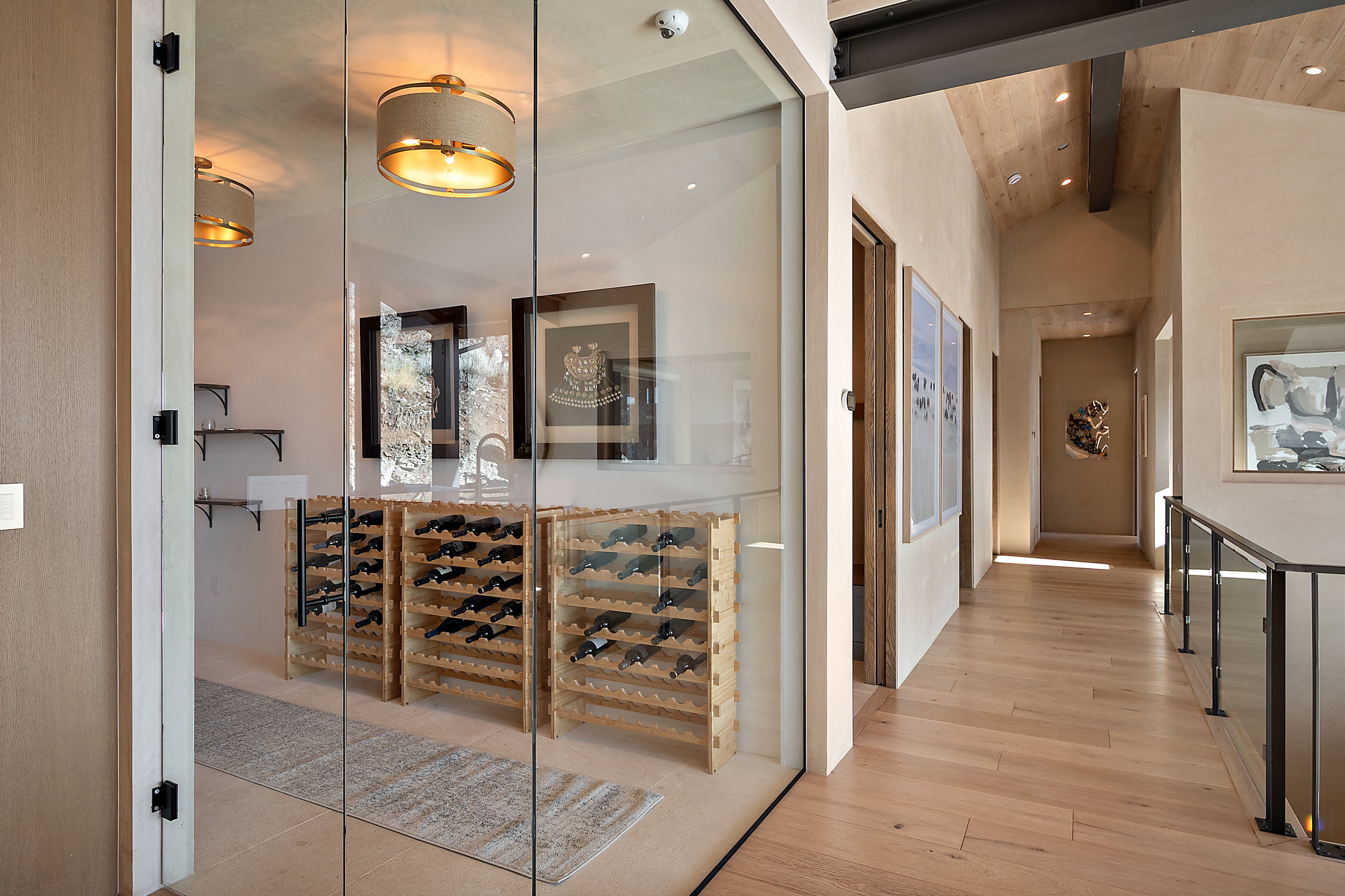 Glass-enclosed wine storage area featuring wood bottle racks, a built-in sink, and decorative lighting fixtures