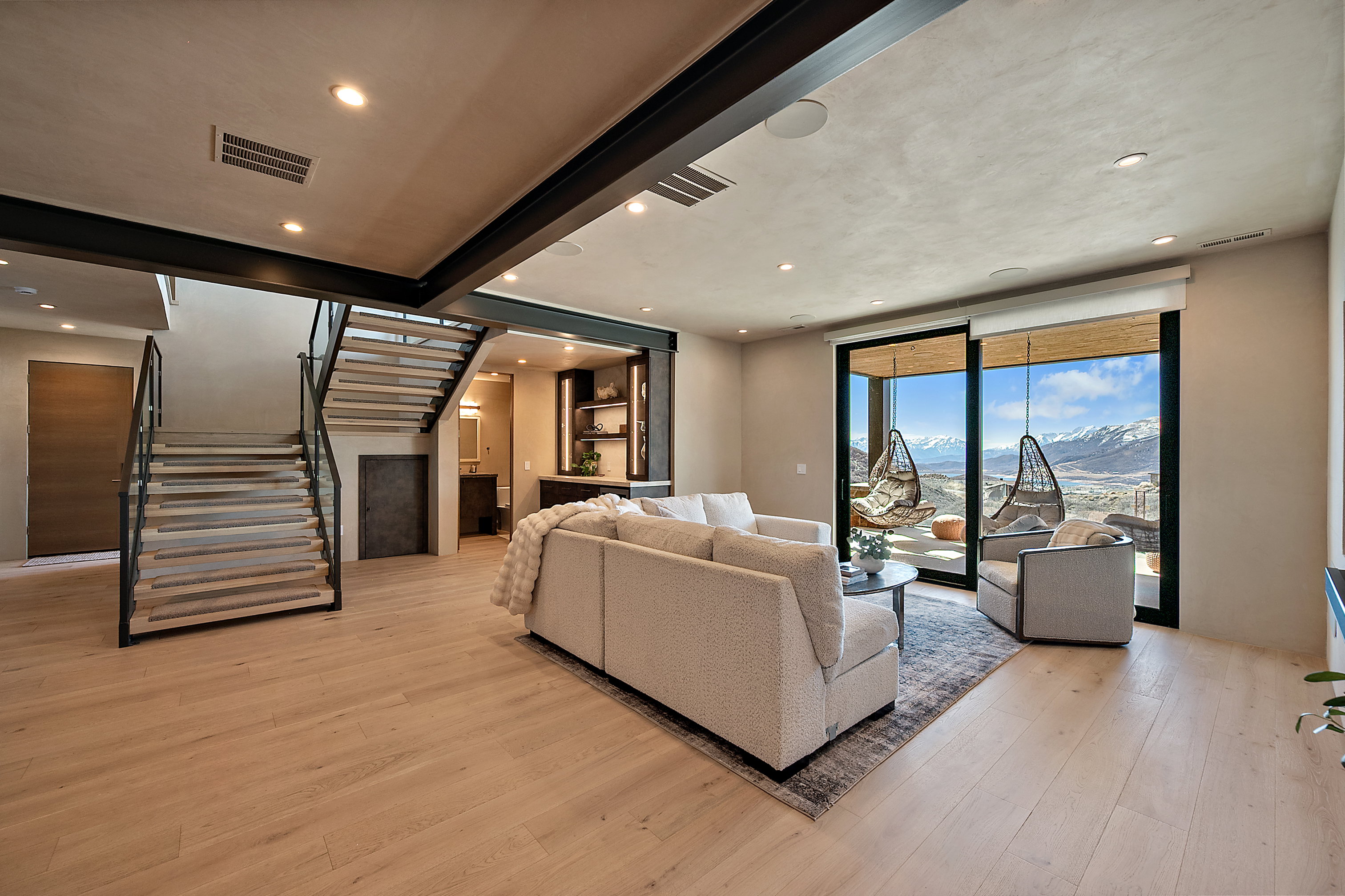 Spacious living area featuring light wood-finish flooring, recessed lighting, and exposed structural beams