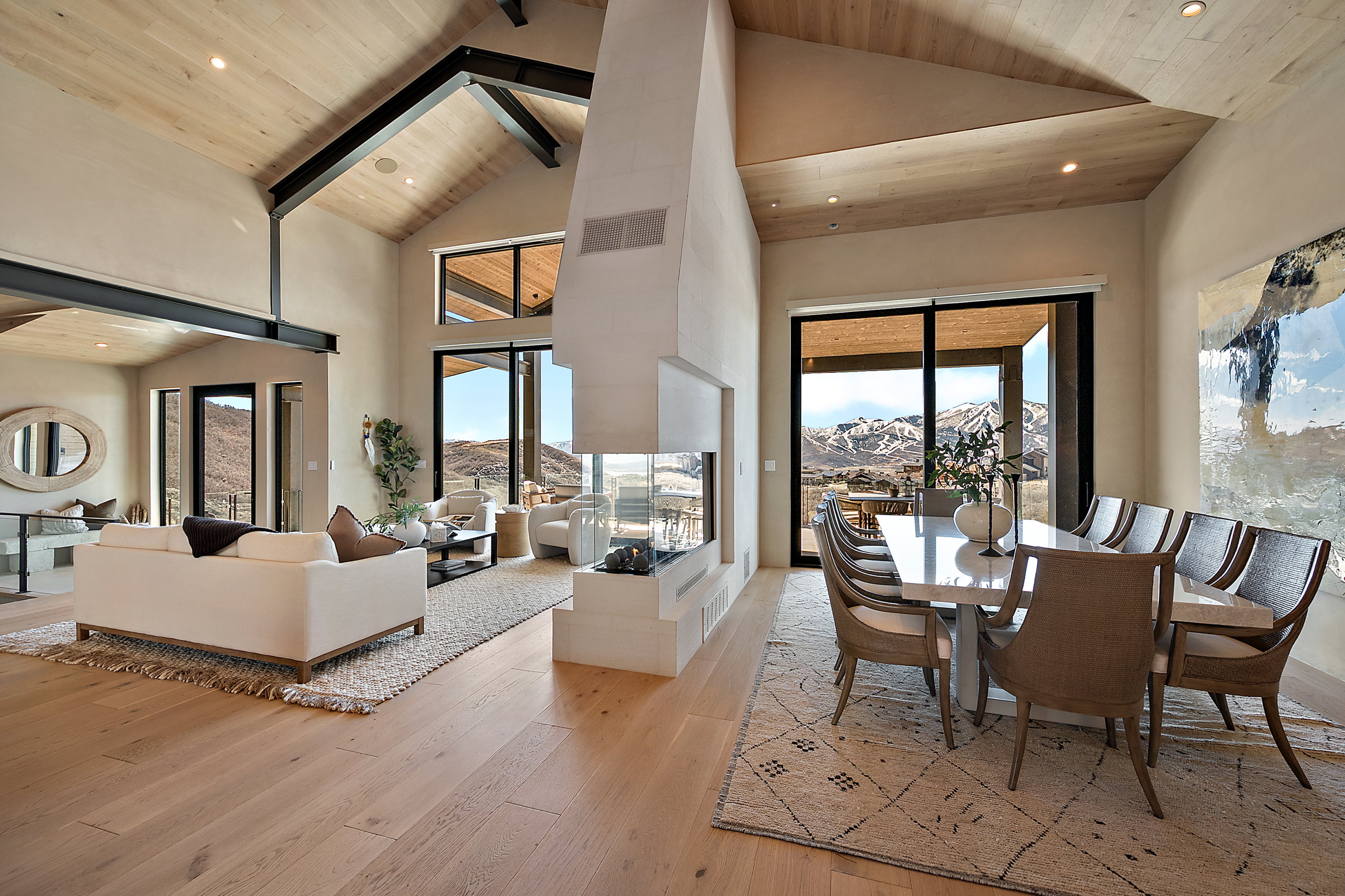 Spacious interior featuring a vaulted wood-paneled ceiling, exposed structural beams, a contemporary fireplace, wood-finish flooring, and expansive sliding glass doors