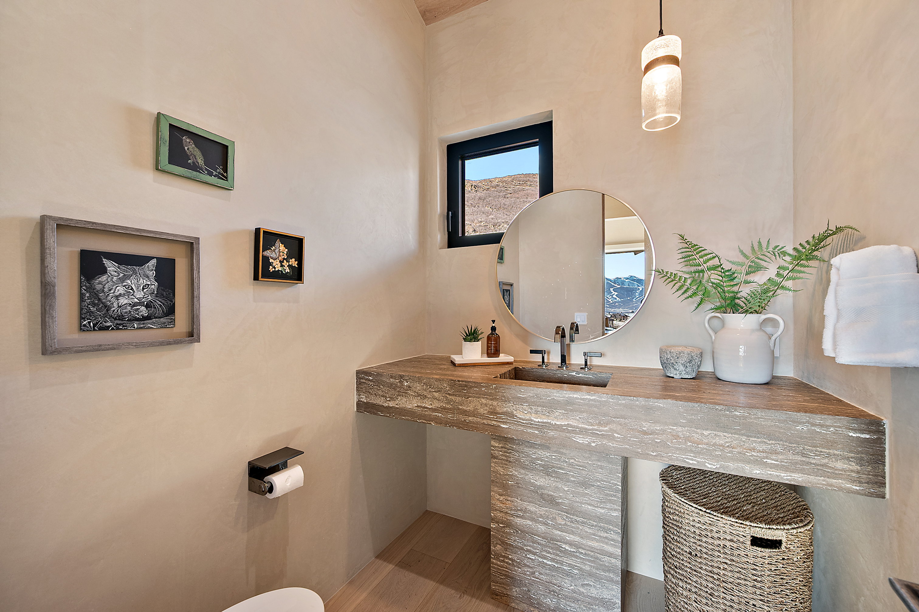 Powder room featuring a stone-finish vanity with an integrated sink, round mirror, and wall-mounted pendant lighting