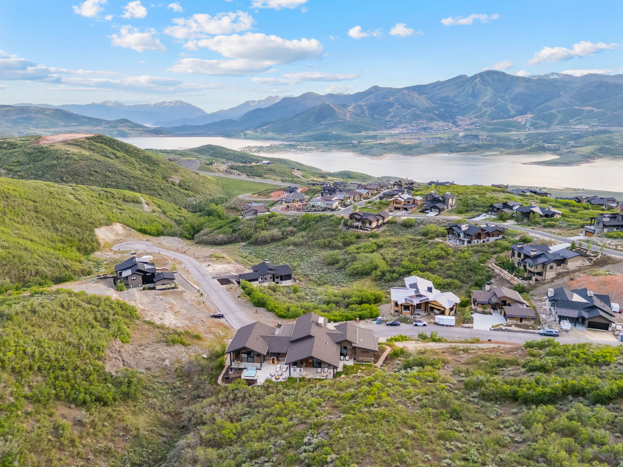 Expansive aerial showcasing multiple properties nestled into a verdant hillside with distant mountain and lake scenery