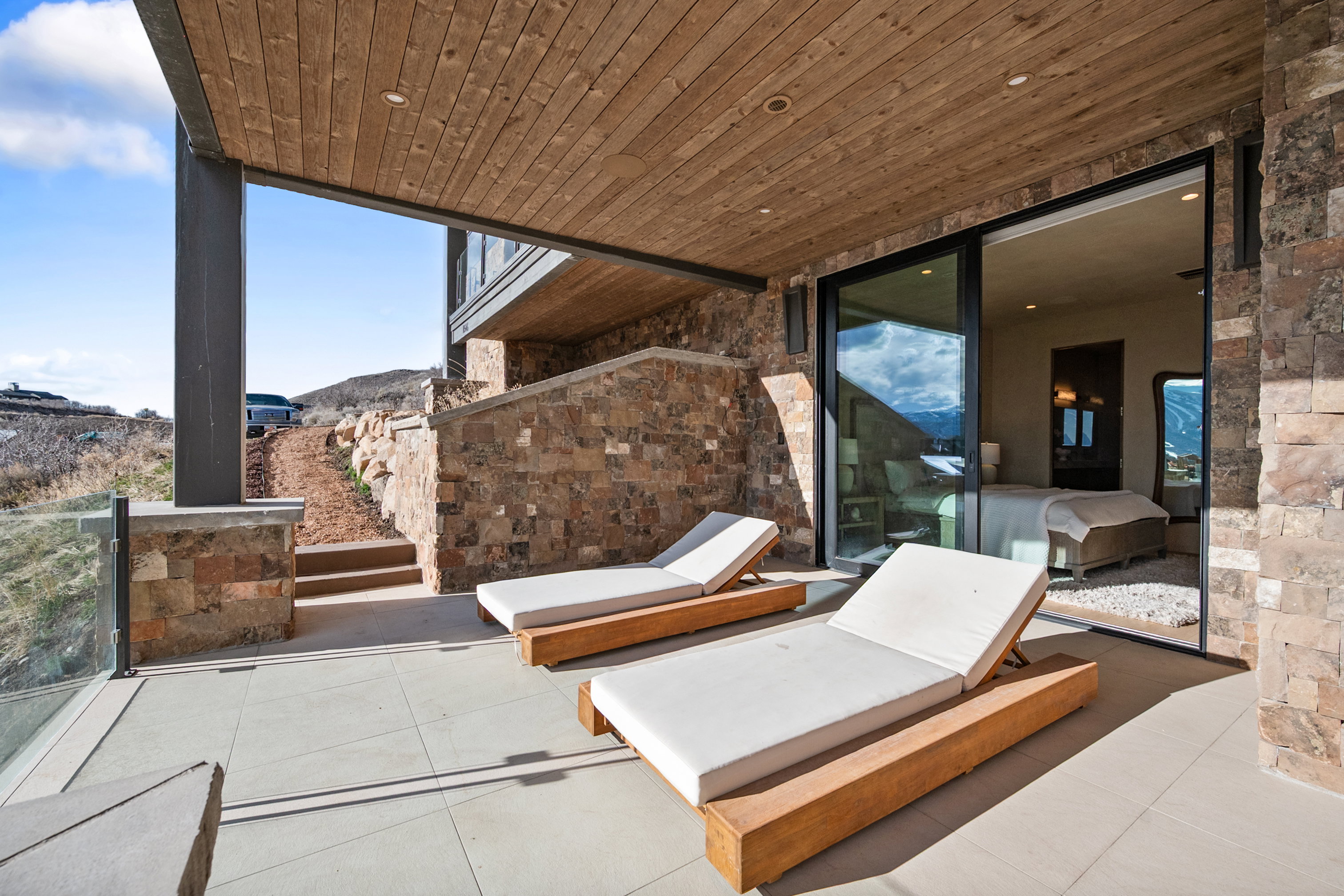 Expansive outdoor patio featuring large format tile flooring, a wood-paneled ceiling, and a glass safety railing
