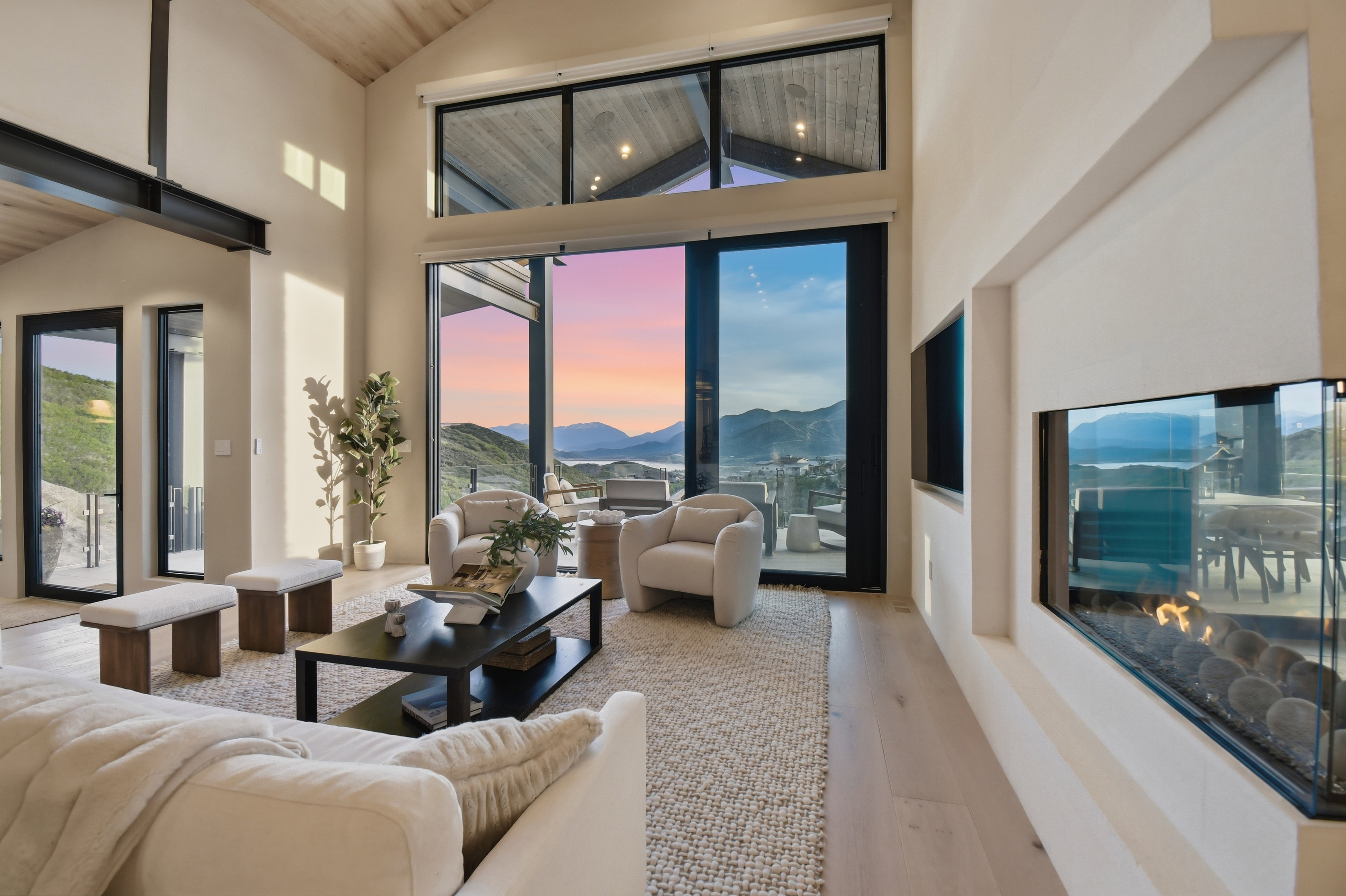 Vaulted ceiling with wood-finish planks, exposed structural beam, wood-finish flooring, floor-to-ceiling sliding glass doors, and a linear gas fireplace with a glass enclosure