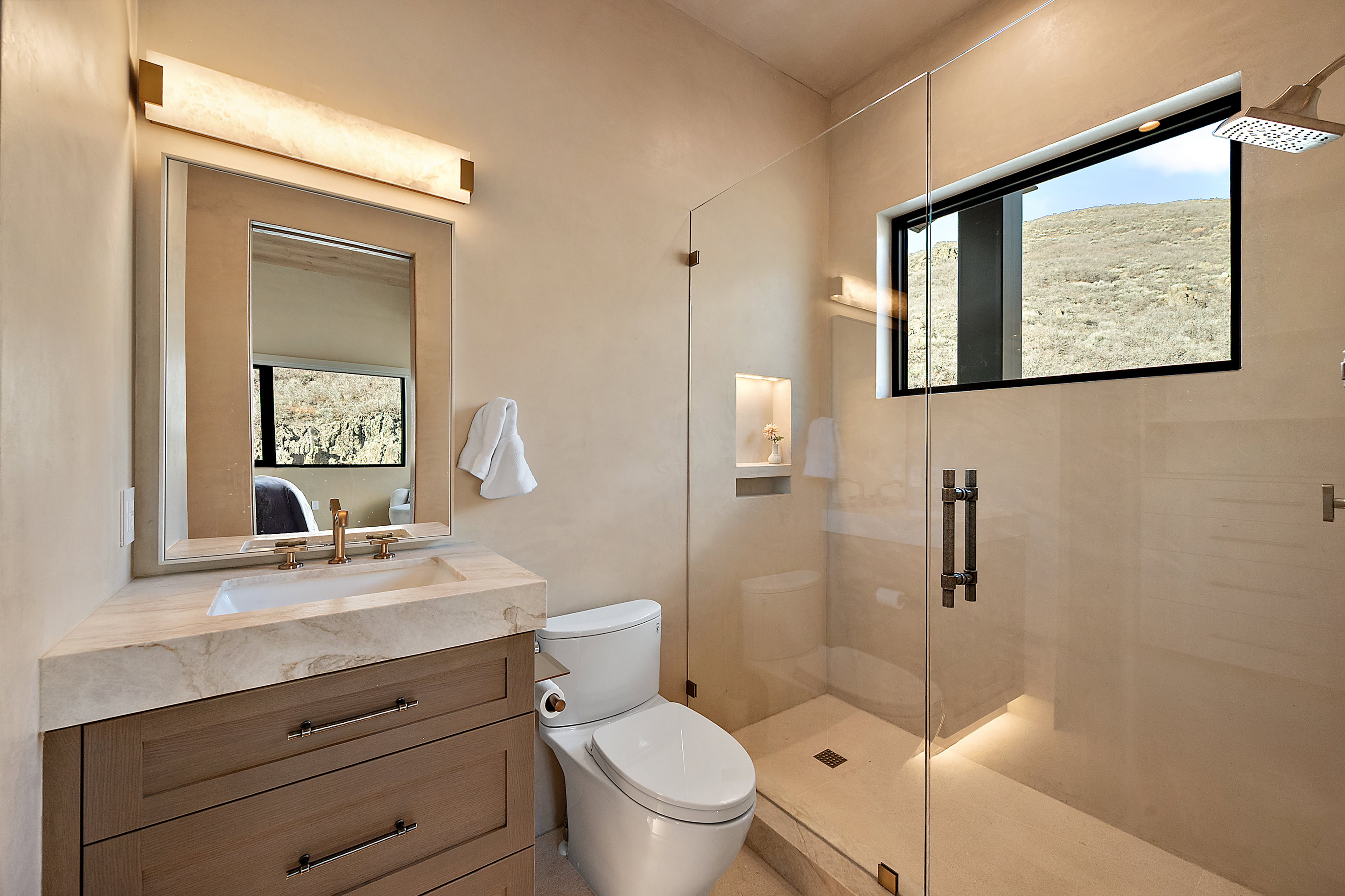 Spacious bathroom featuring a frameless glass shower enclosure with a rainfall showerhead, a built-in shower niche with accent lighting, and a linear window