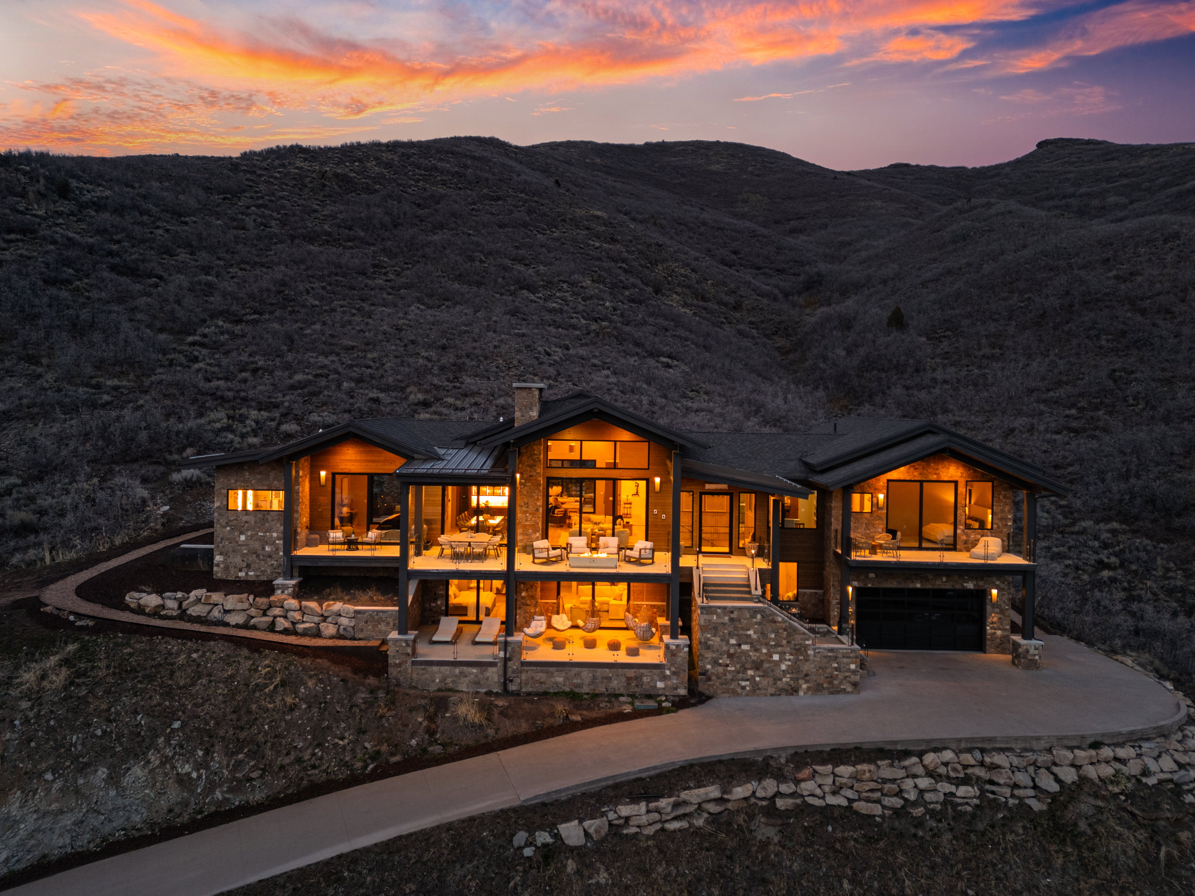 Contemporary mountain-style residence featuring extensive stone veneer, dark wood siding, multiple expansive balconies, a two-car garage, and a concrete driveway