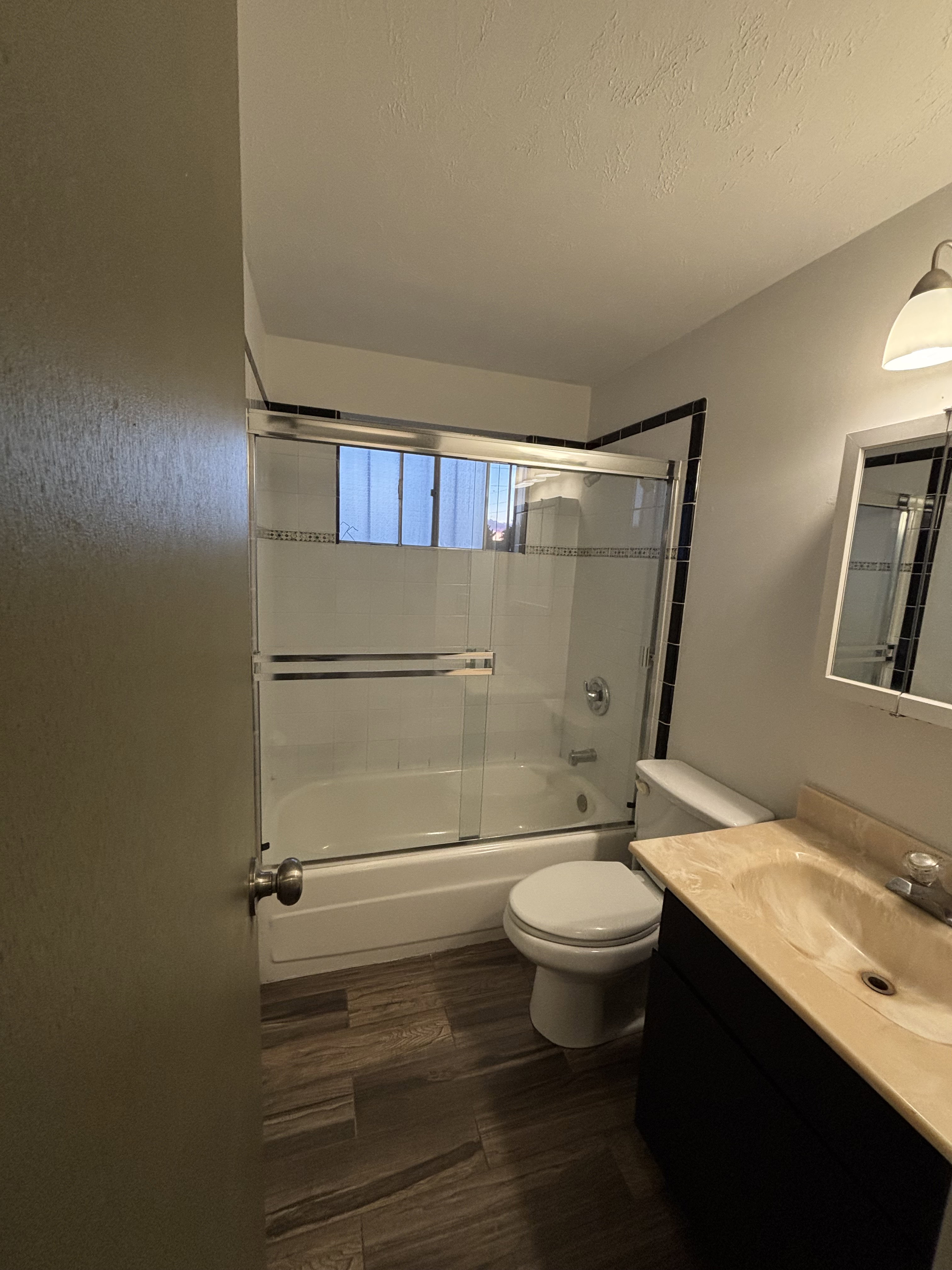 Bathroom featuring a tub/shower combination with sliding glass doors, a vanity with a light-toned countertop, dark wood-finish flooring, and a wall-mounted light fixture