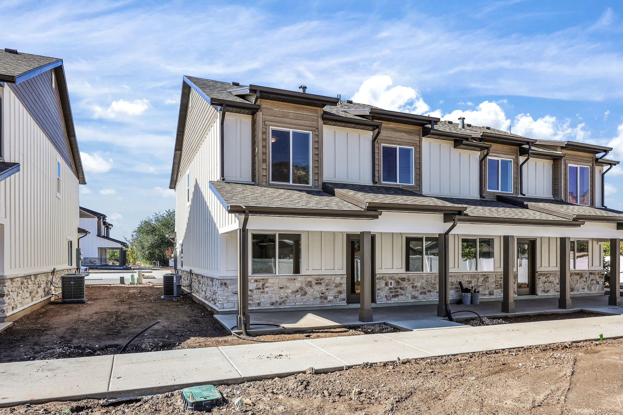 Contemporary townhome exterior featuring vertical white siding, stone veneer accents, and dark trim